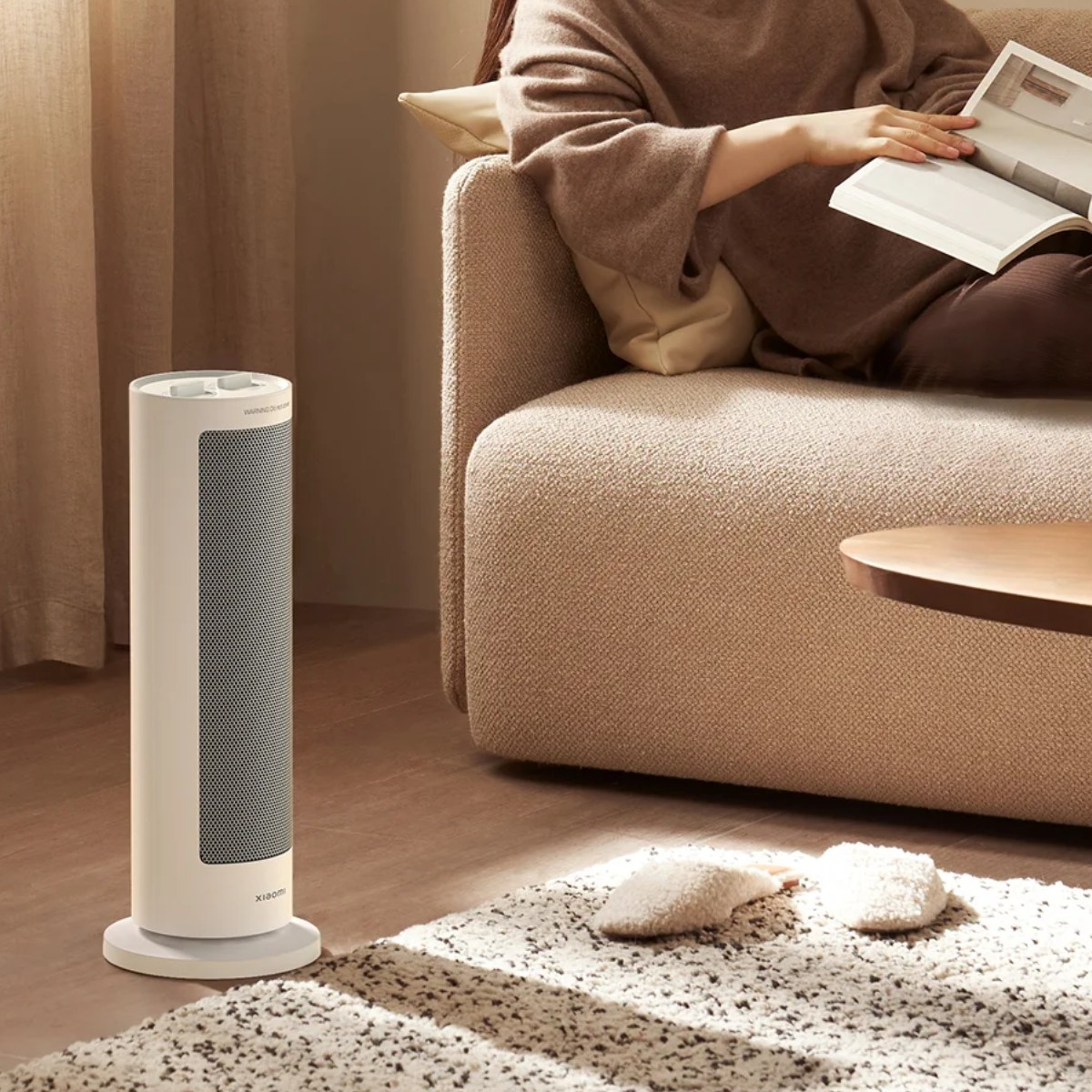 Osoba czyta na sofie obok białego grzejnika. Na podłodze leżą dywan i kapcie.