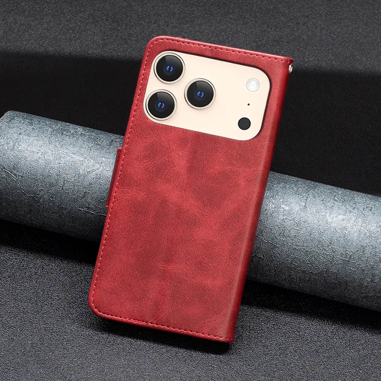 Een rode leren telefoonhoes met drie cameralenzen. Het ligt op een getextureerd donker oppervlak met een grijs cilindrisch object erachter.