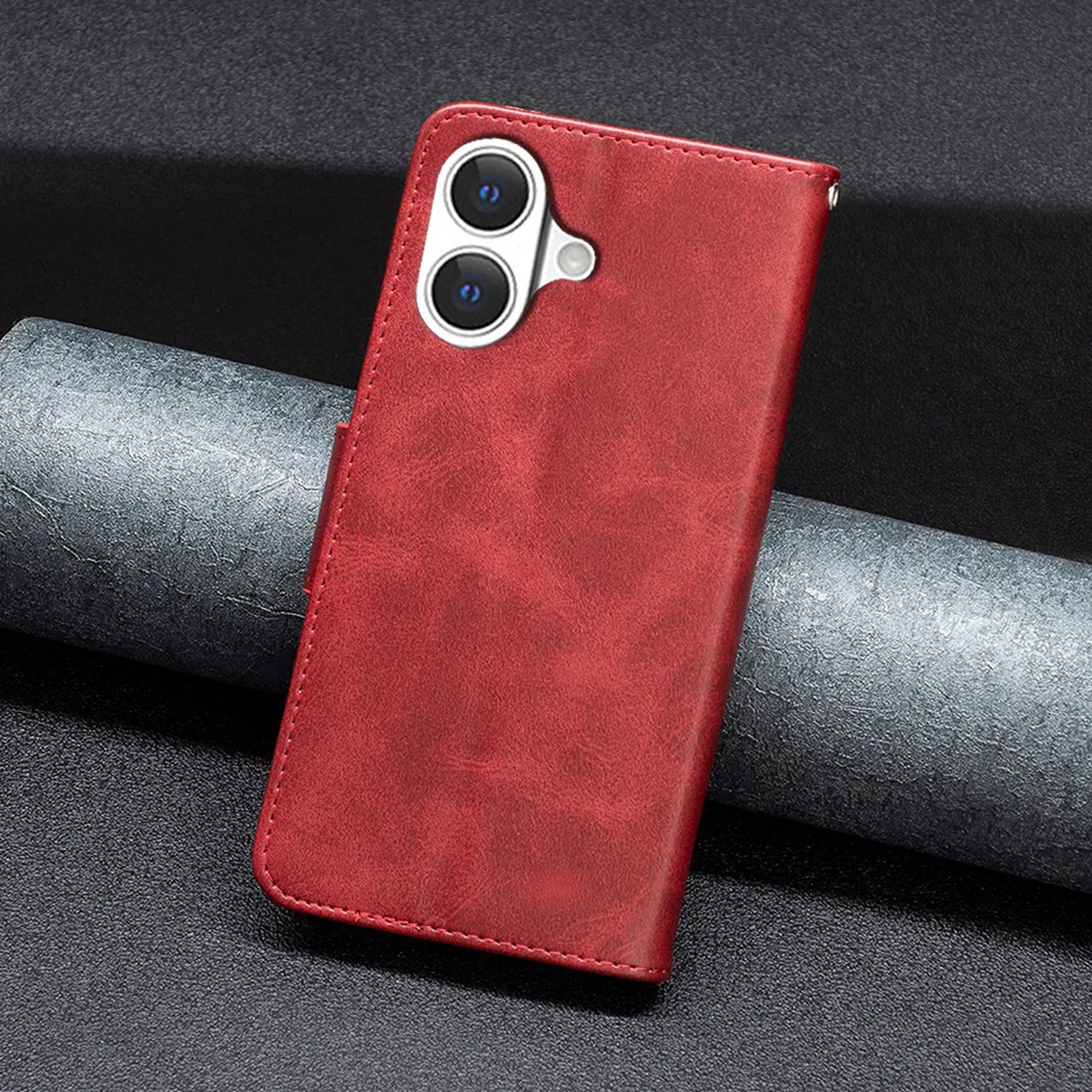 Een rode leren telefoonhoes, met twee cameralenzen, ligt op een donker ge textuurd oppervlak. Een grijs opgerold object staat op de achtergrond.