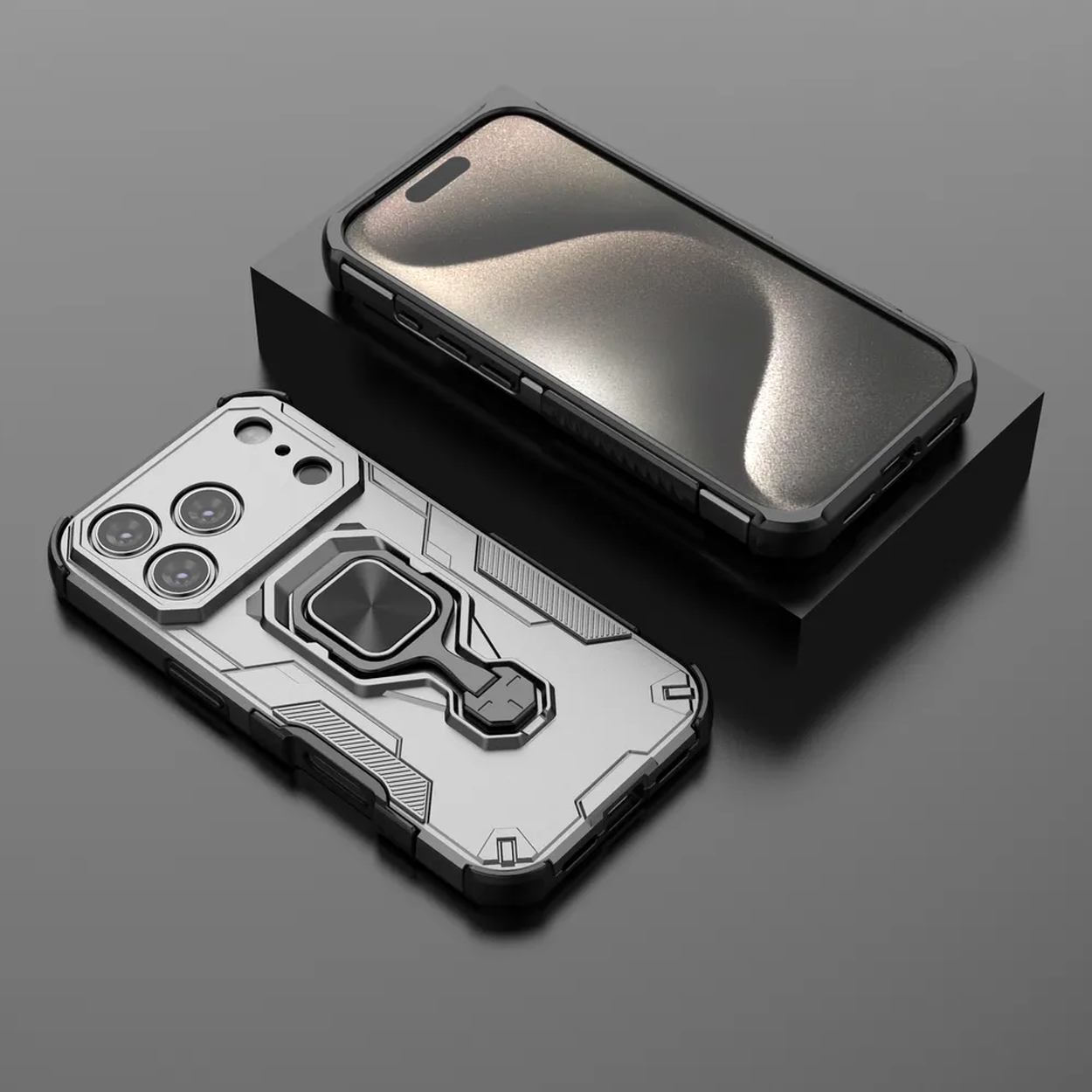 Twee telefoonhoesjes, een op een zwart blok. Beide zijn zilver en zwart, met camera-uitsparingen en een ringhouder. Zwarte achtergrond.