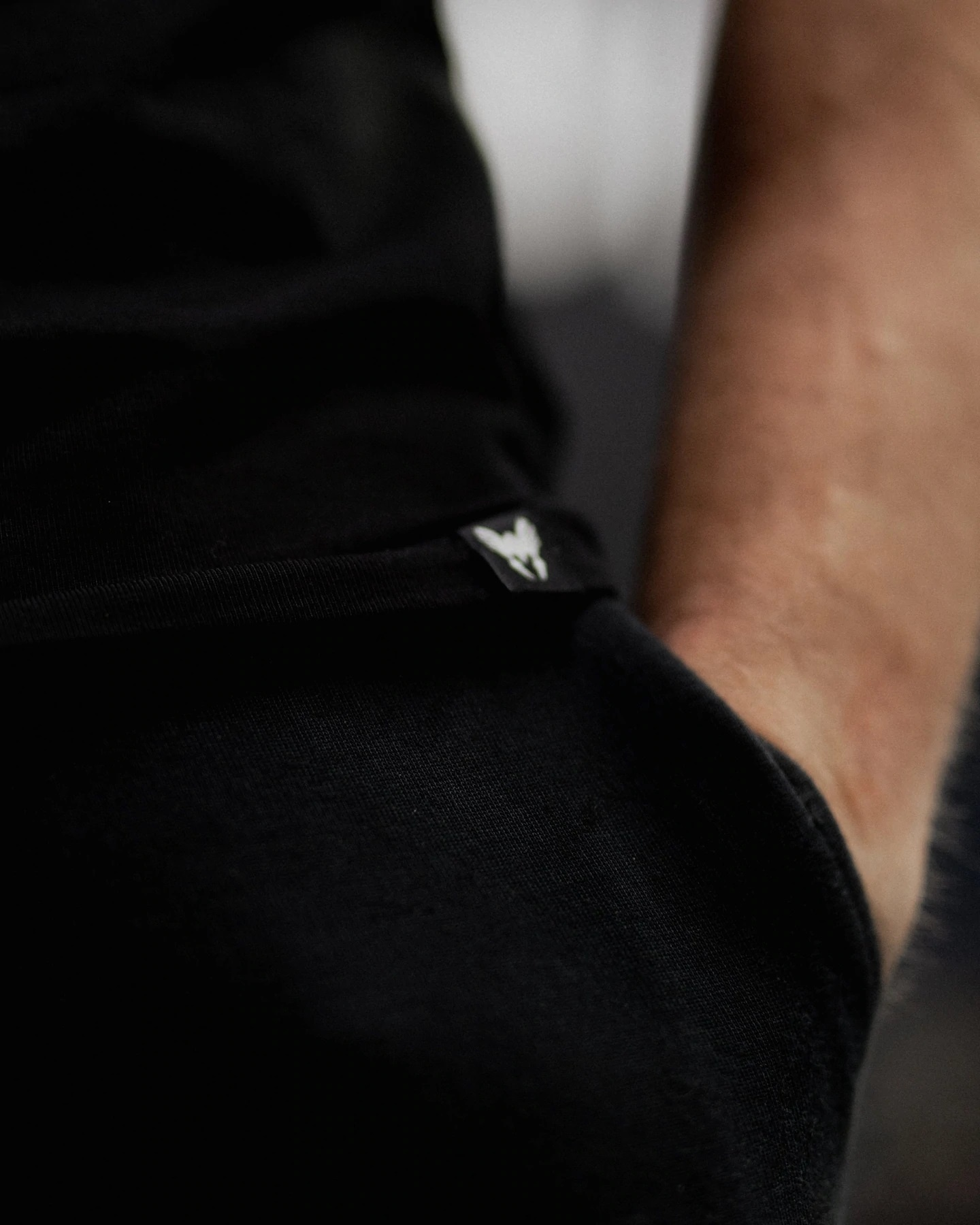 Close-up van de arm en het zwarte shirt van een persoon. Er staat een klein wit logo op het shirt. Huidskleur is zichtbaar.