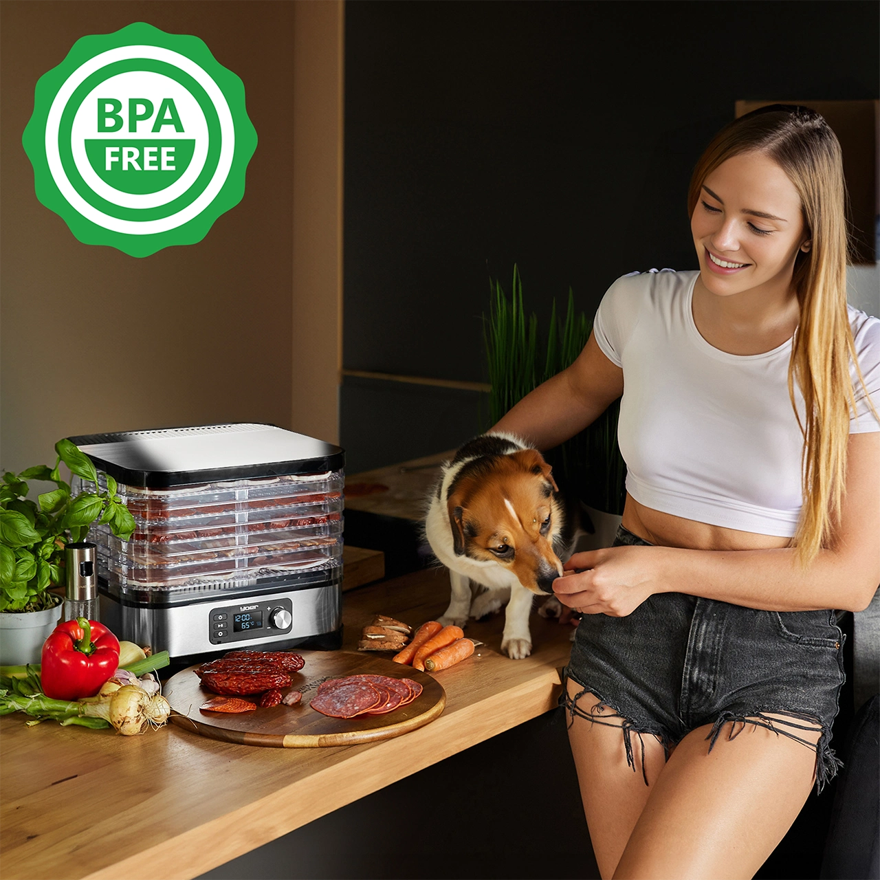 Kobieta i pies w pobliżu suszarki do żywności. Jedzenie i warzywa na stole. Logo wolne od BPA.