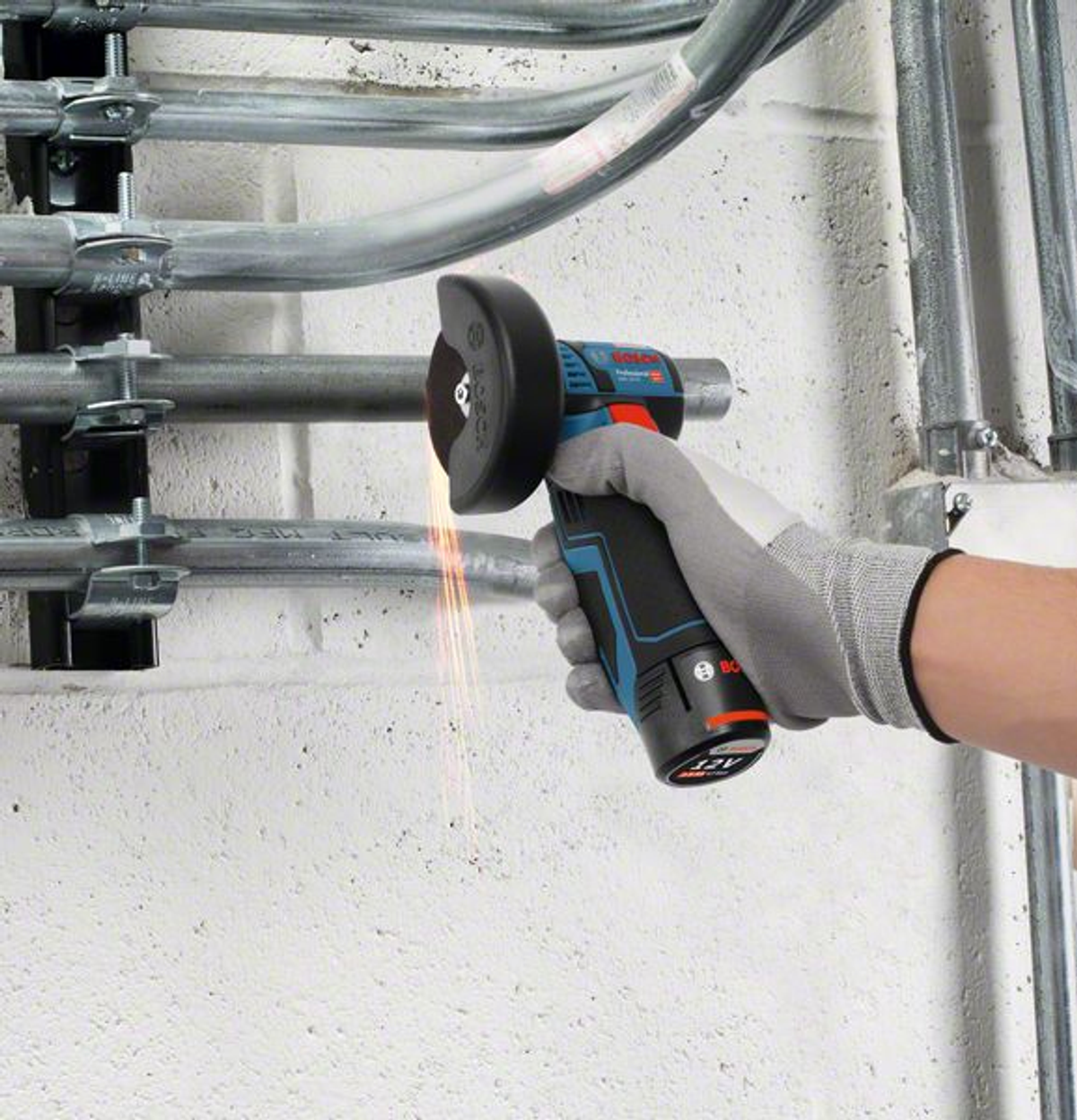 Osoba używa szlifierki do cięcia metalowej rury. Iskry lecą z tarczy tnącej. Ręka w rękawicy trzyma narzędzie.