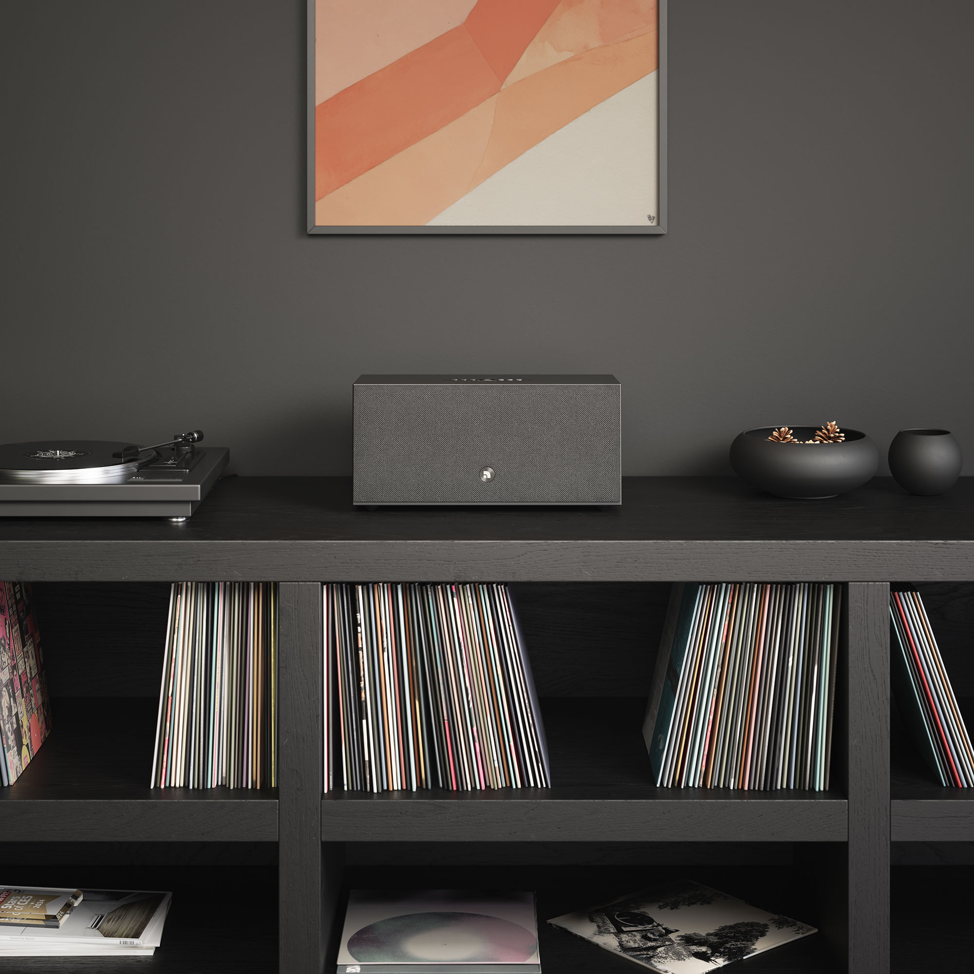 Ein schwarzes Regal mit Plattenspieler, Lautsprecher und Schallplatten. Ein Kunstwerk hängt darüber.