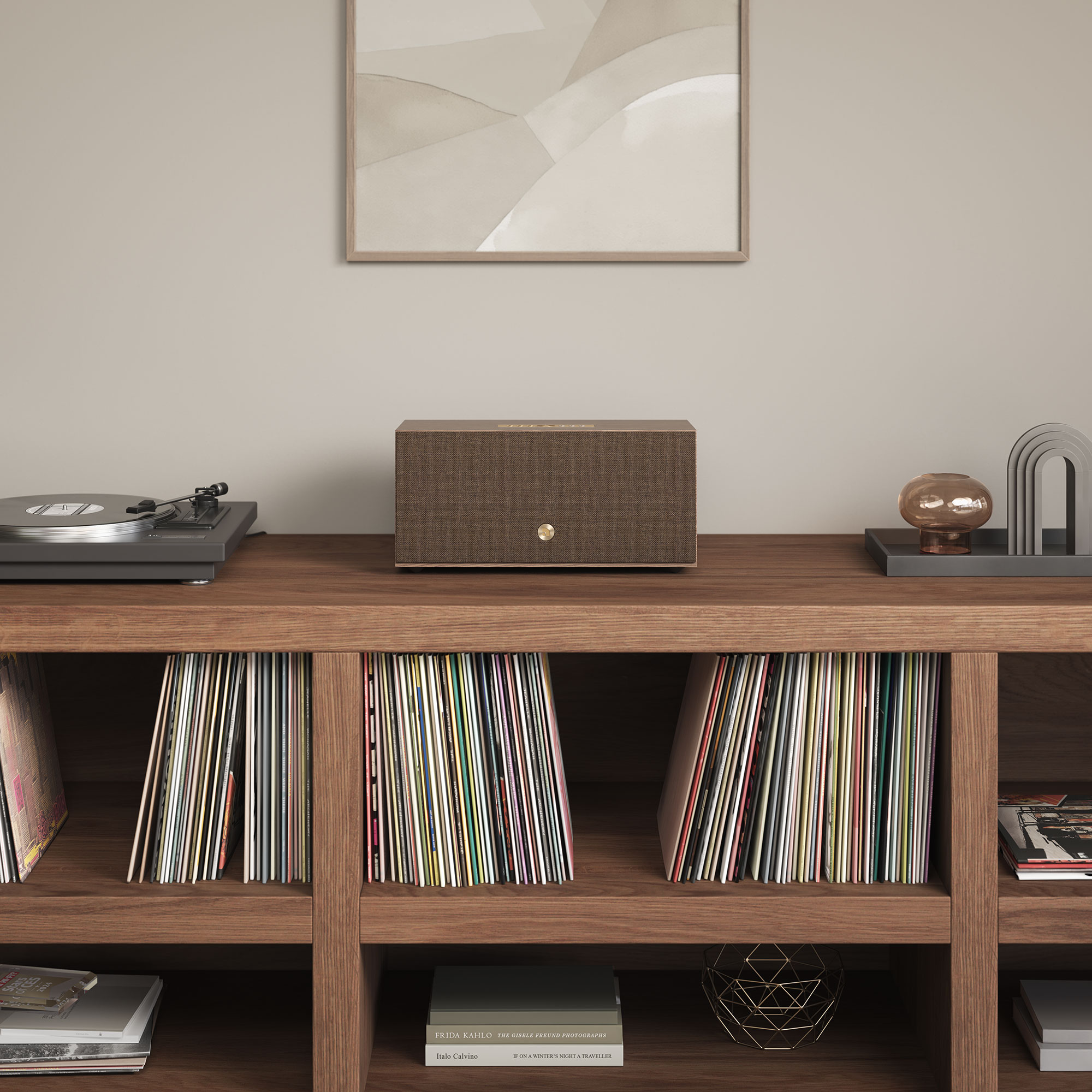 Ein Holzschrank mit Schallplatten, einem Plattenspieler und einem Lautsprecher. An der Wand hängt ein gerahmtes Gemälde. Dekorative Gegenstände stehen auf dem Schrank.