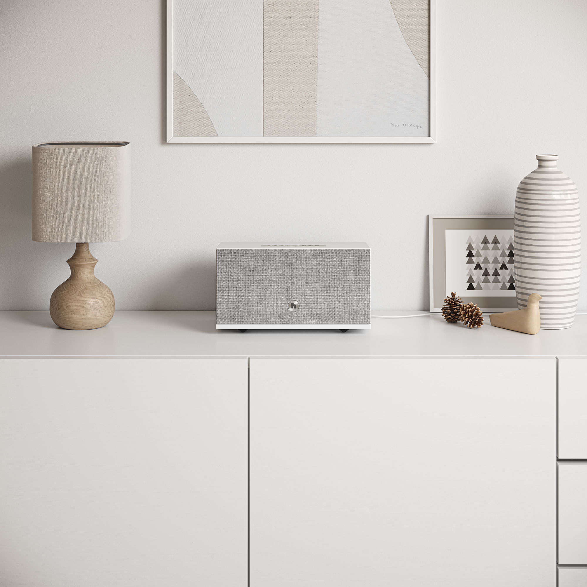 Ein weißer Schrank mit Lautsprecher, Lampe, Kunst, Vase und Dekor. Der Lautsprecher befindet sich vor dem Schrank. Beige Wand.