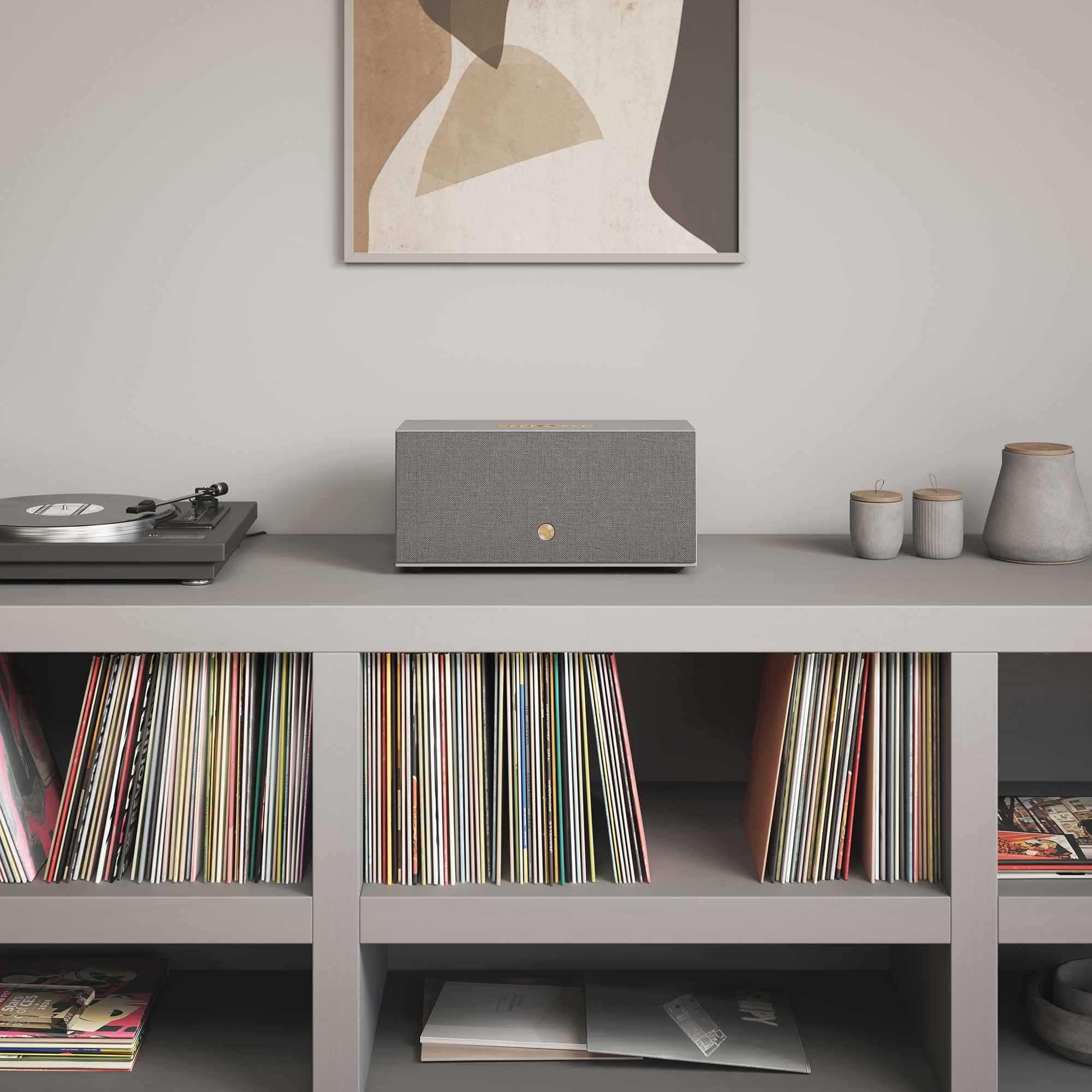 Graues Regal mit Plattenspieler, Lautsprecher und Deko-Artikeln. Schallplatten füllen die unteren Regale. Abstrakte Kunst hängt darüber.