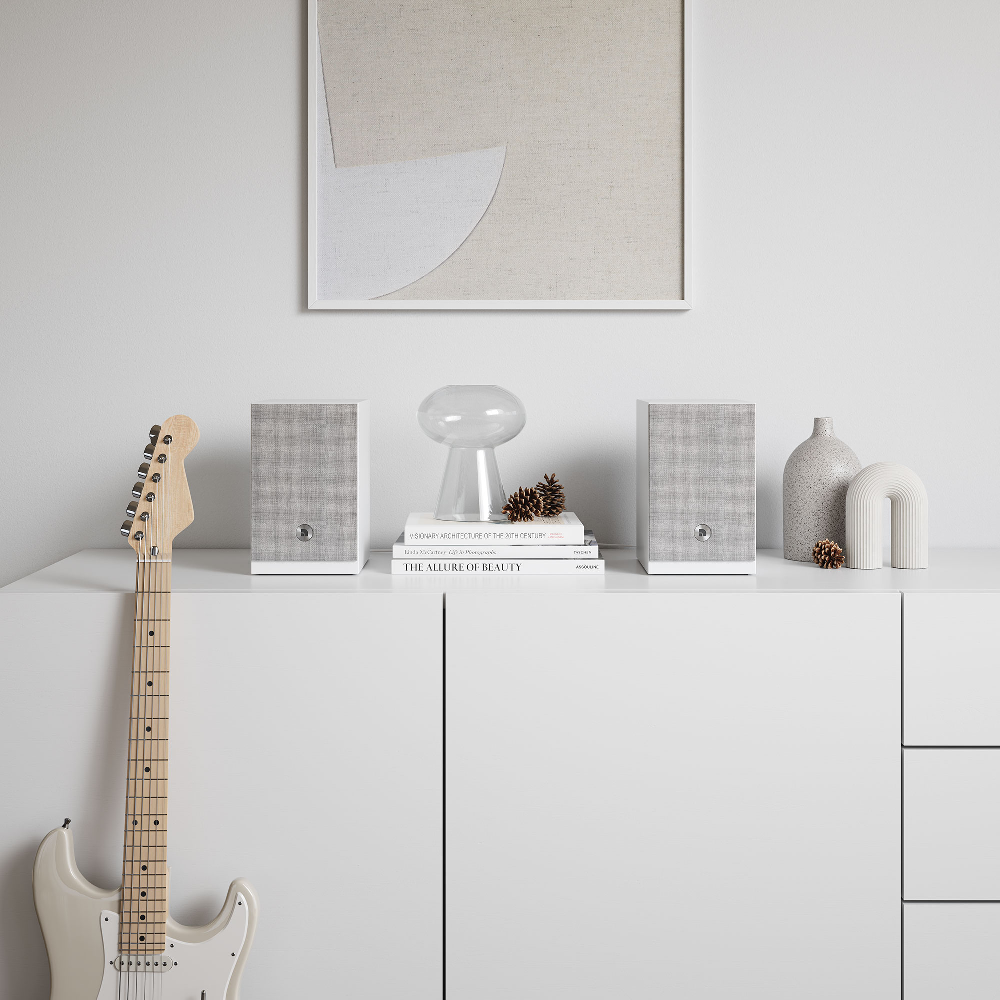 Weißer Schrank mit Lautsprechern, Büchern, Dekor und Gitarre. Ein gerahmtes abstraktes Kunstwerk hängt darüber.