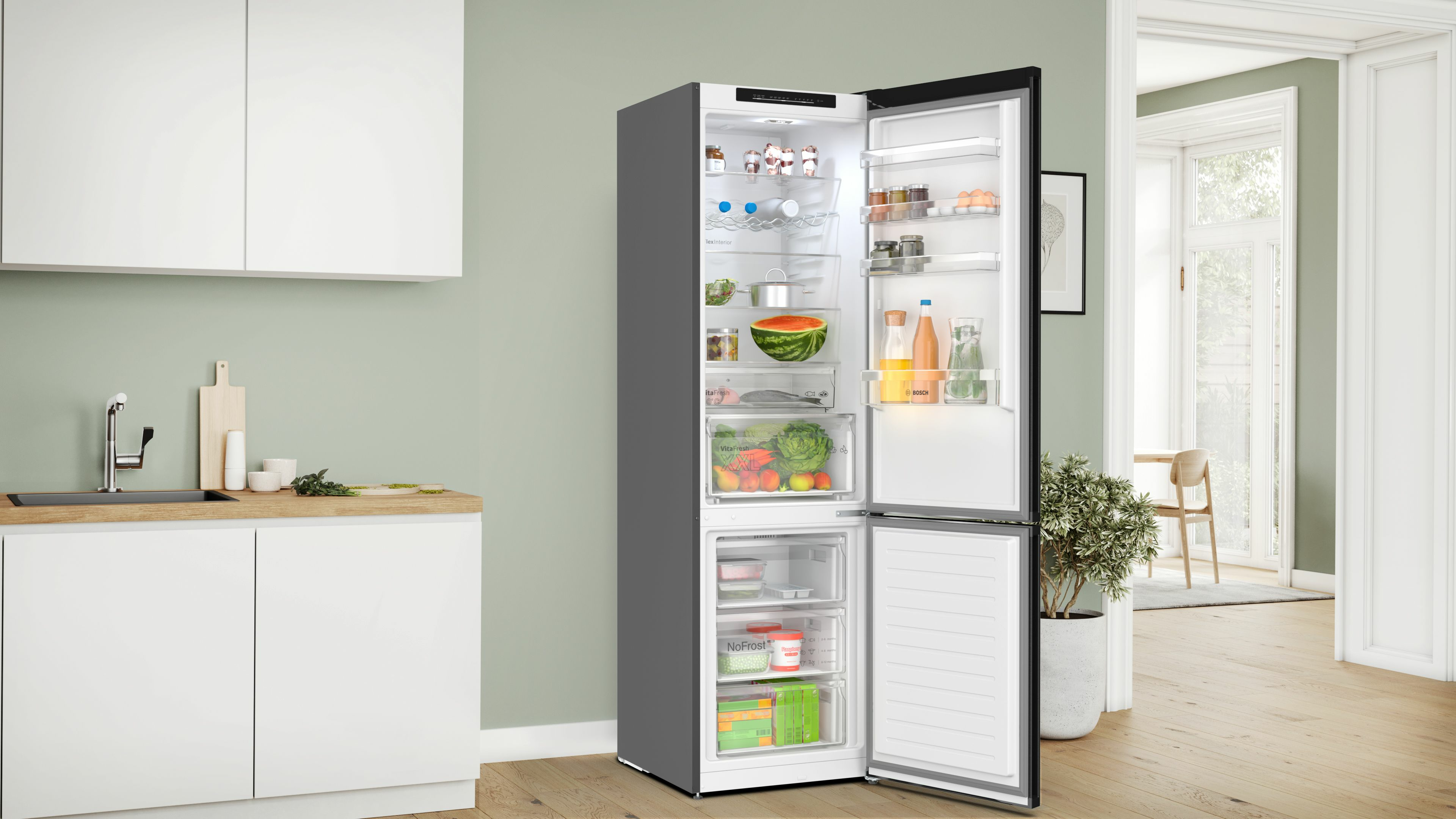 Ein offener Kühlschrank voller Lebensmittel. Eine Küchenzeile und eine Pflanze im Topf sind im Hintergrund.