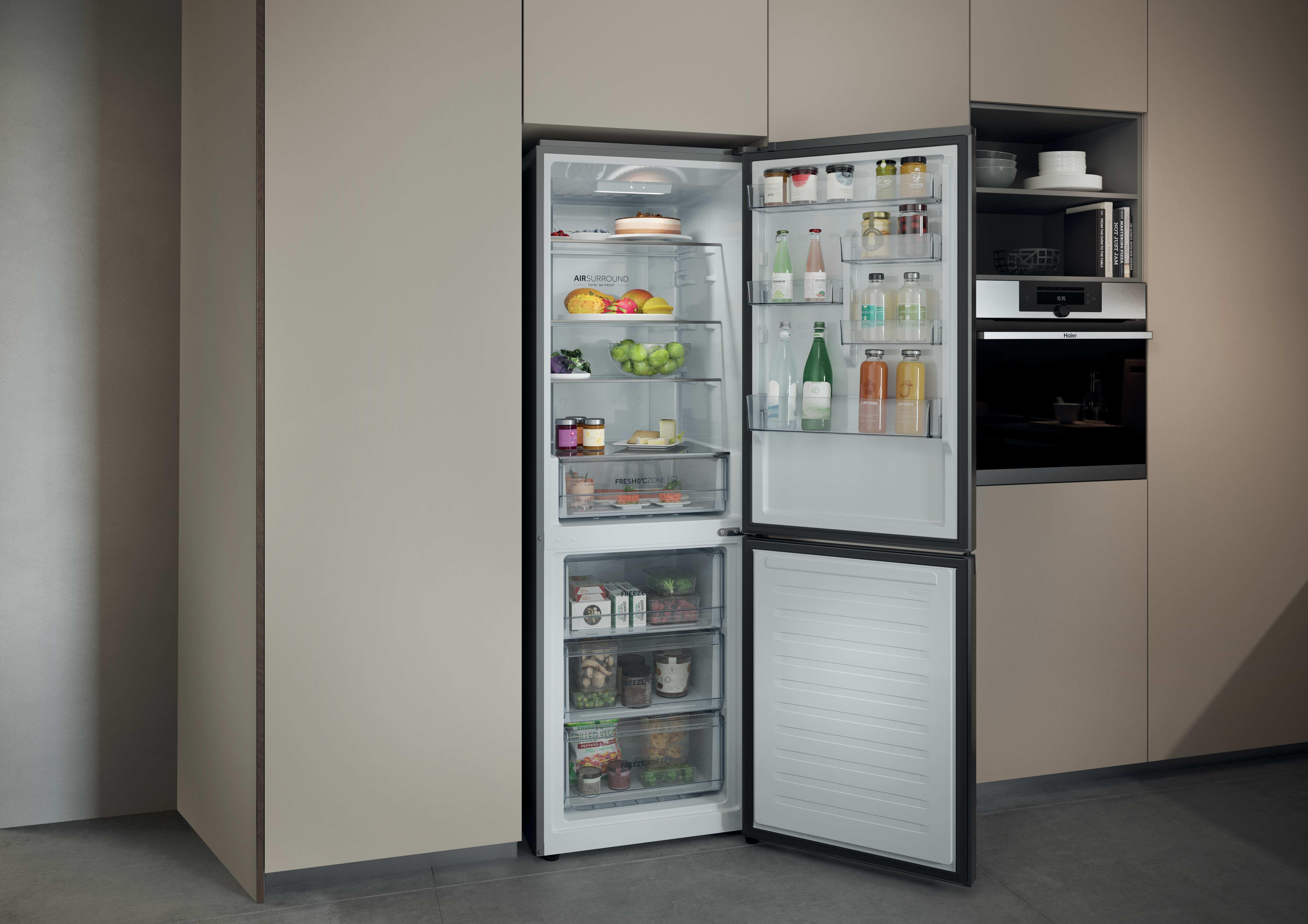 Otwarta lodówka z jedzeniem w środku. Sąsiedni piekarnik i szafki. Widoczne owoce, warzywa, słoiki i napoje.