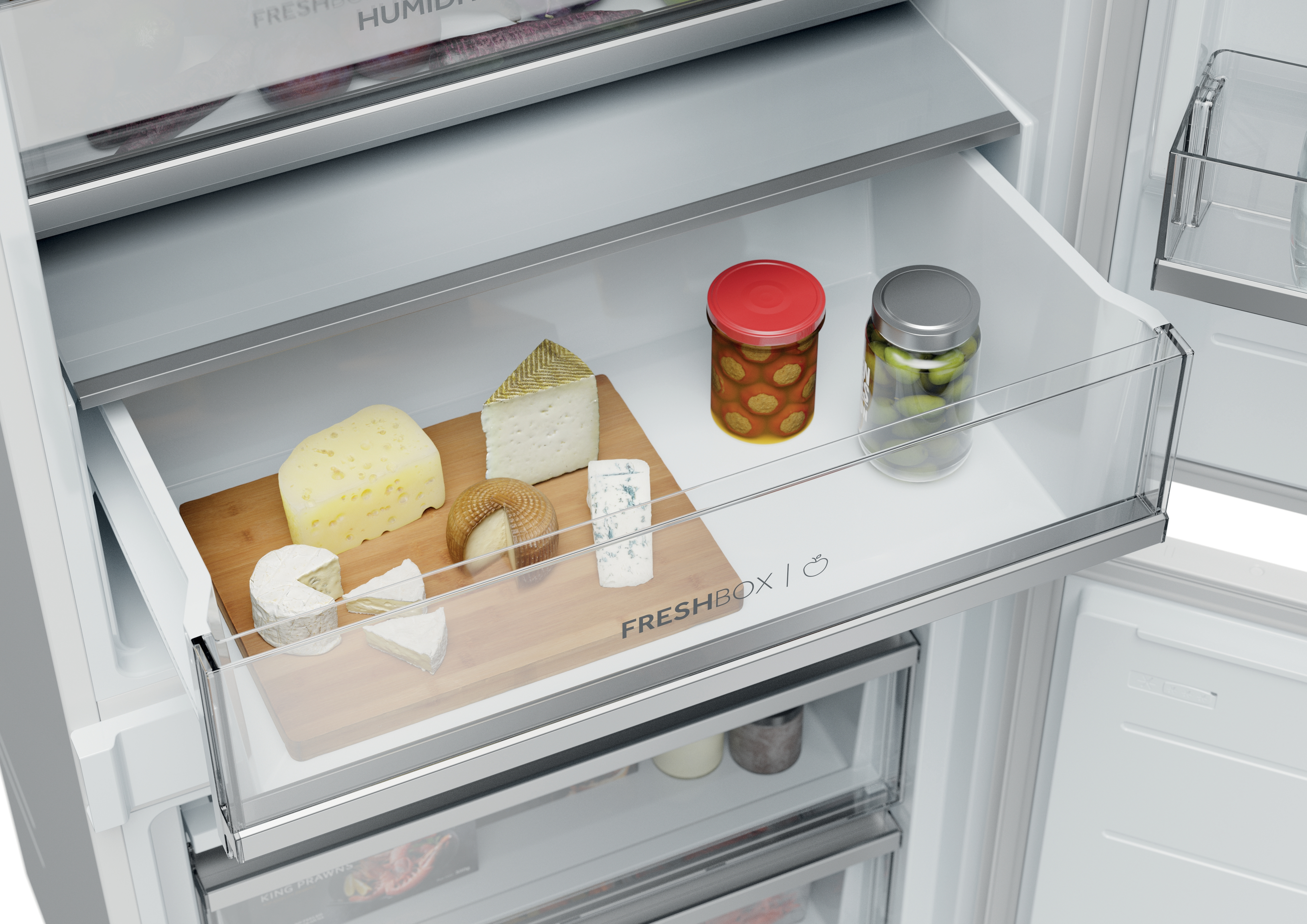 Un cajón de refrigerador con varios quesos en una tabla de madera y frascos de aceitunas y pepinillos.