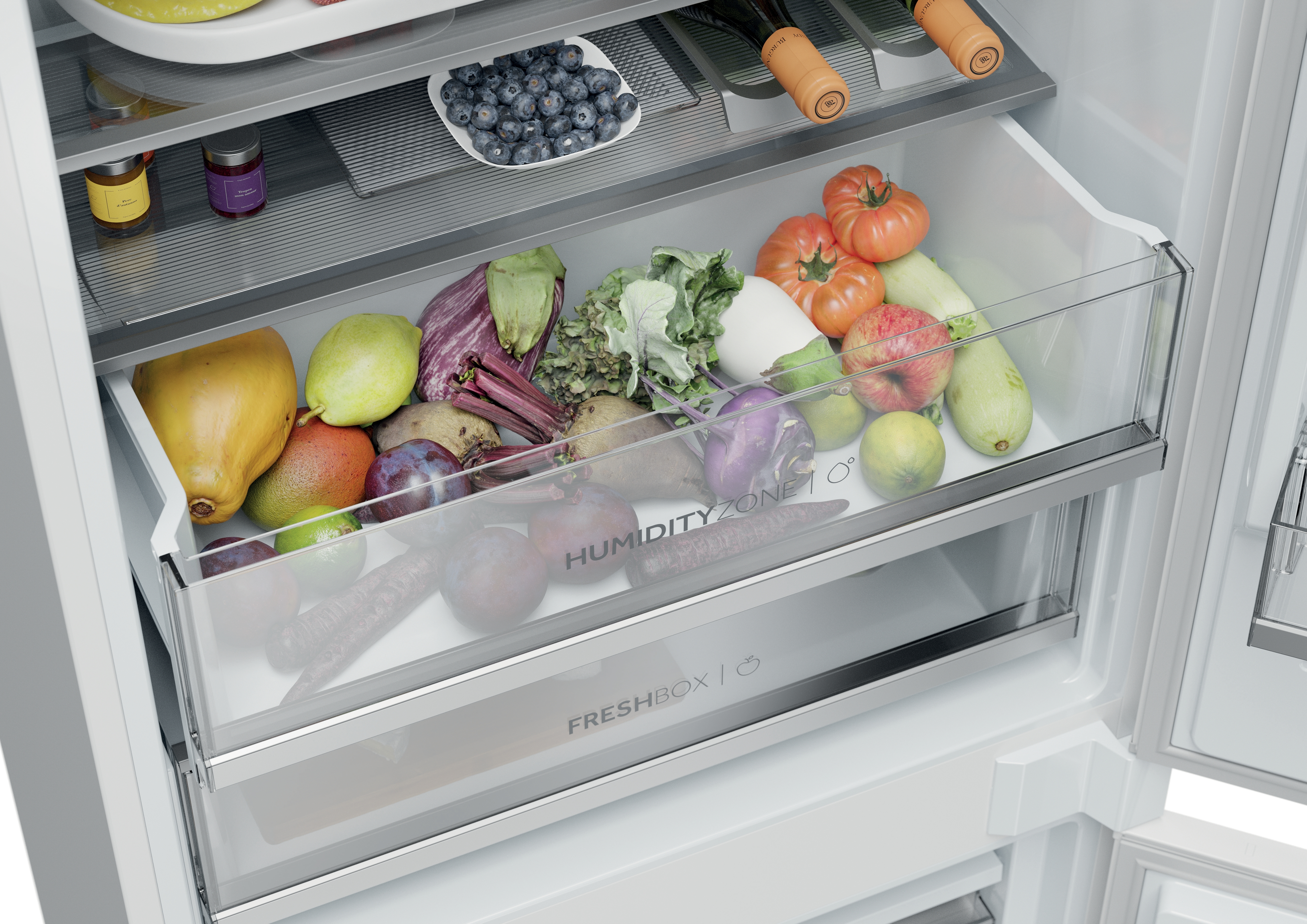Refrigerador abierto con frutas y verduras en cajones. Se ven tomates, manzanas, ciruelas y más.