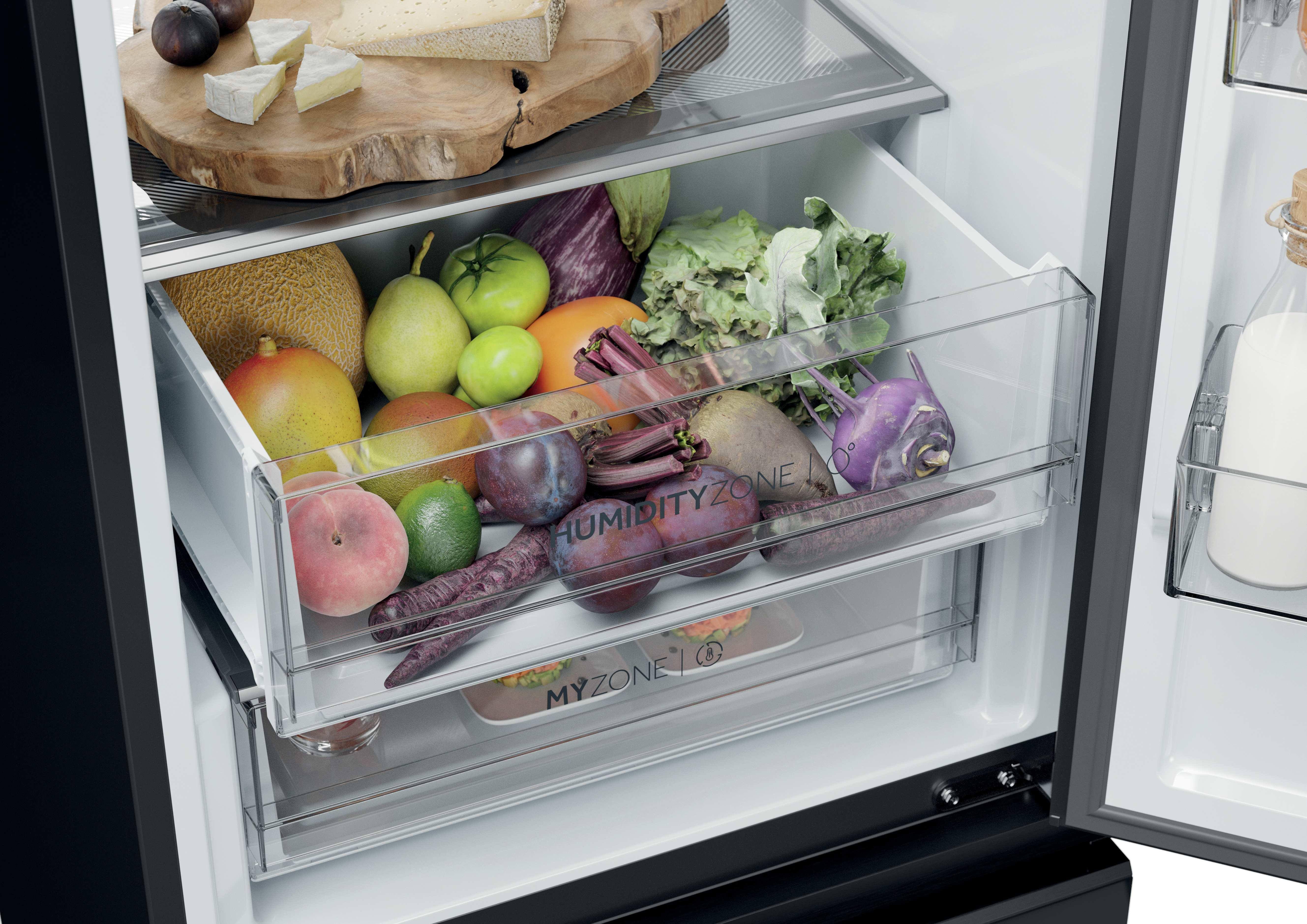 Refrigerador abierto con frutas y verduras en cajones. Queso e higos en una tabla de madera en la parte superior.
