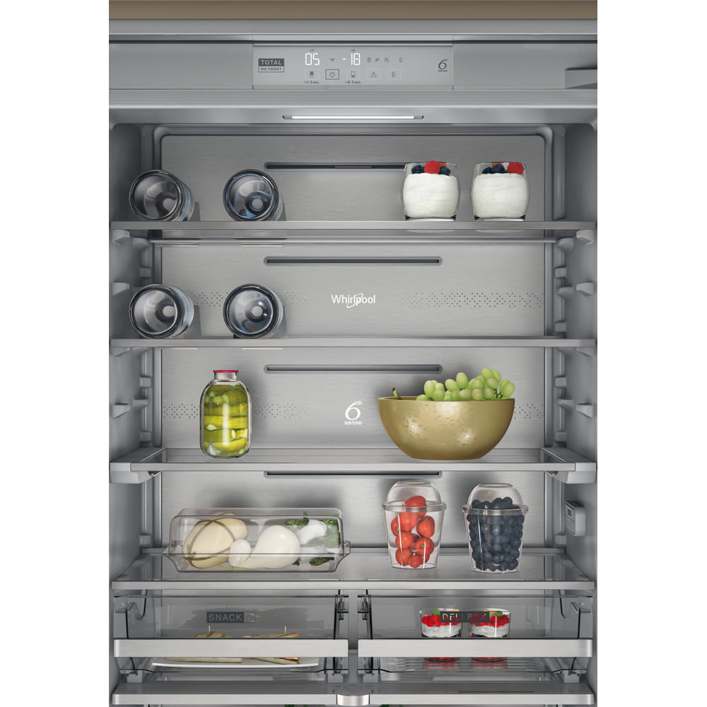 Interno di un frigorifero pieno di cibo. Include bottiglie di vino, yogurt, un barattolo, uva, pomodori, mirtilli e formaggio.