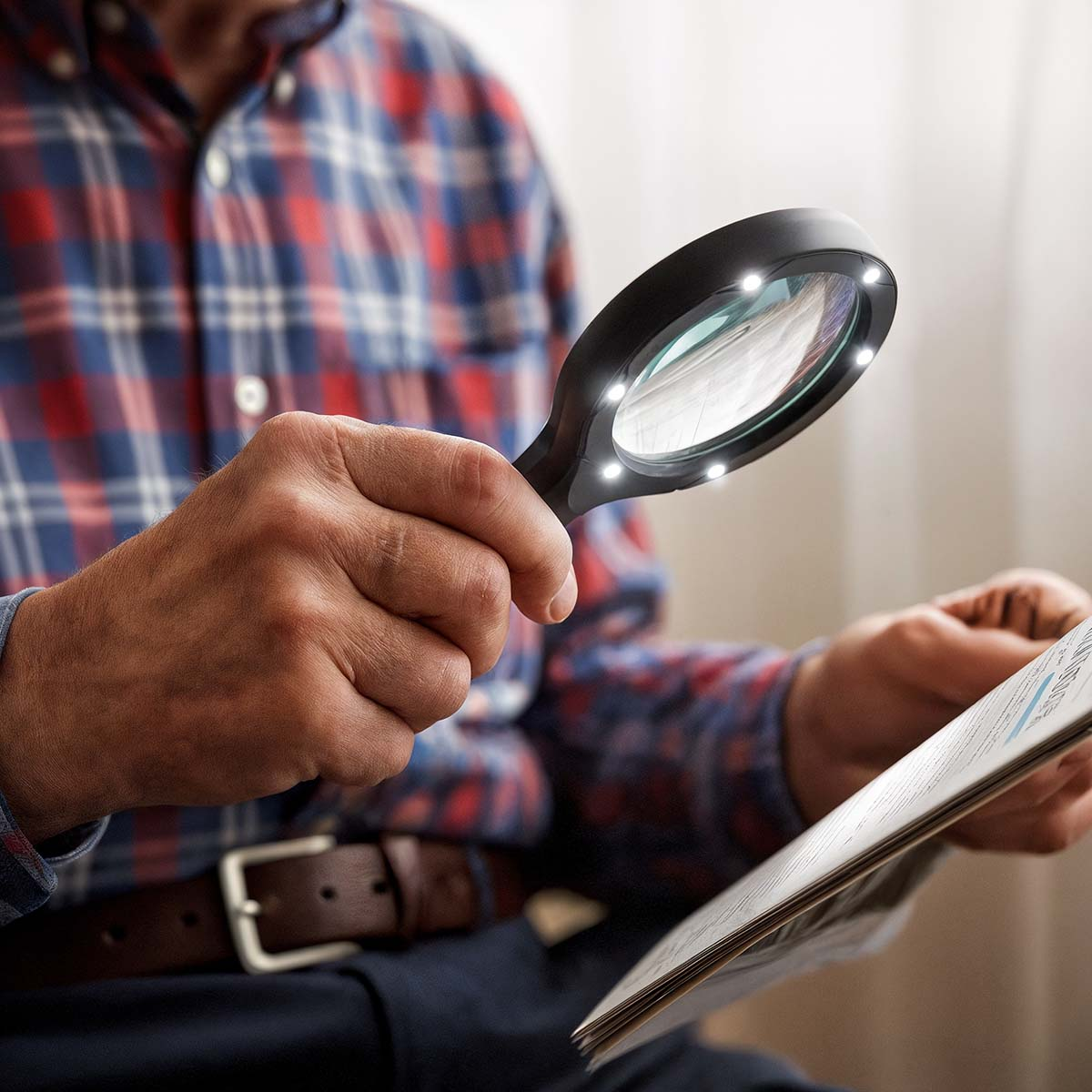 Een man in een geruit overhemd leest een krant met een vergrootglas. Het glas heeft lampjes rond de lens.