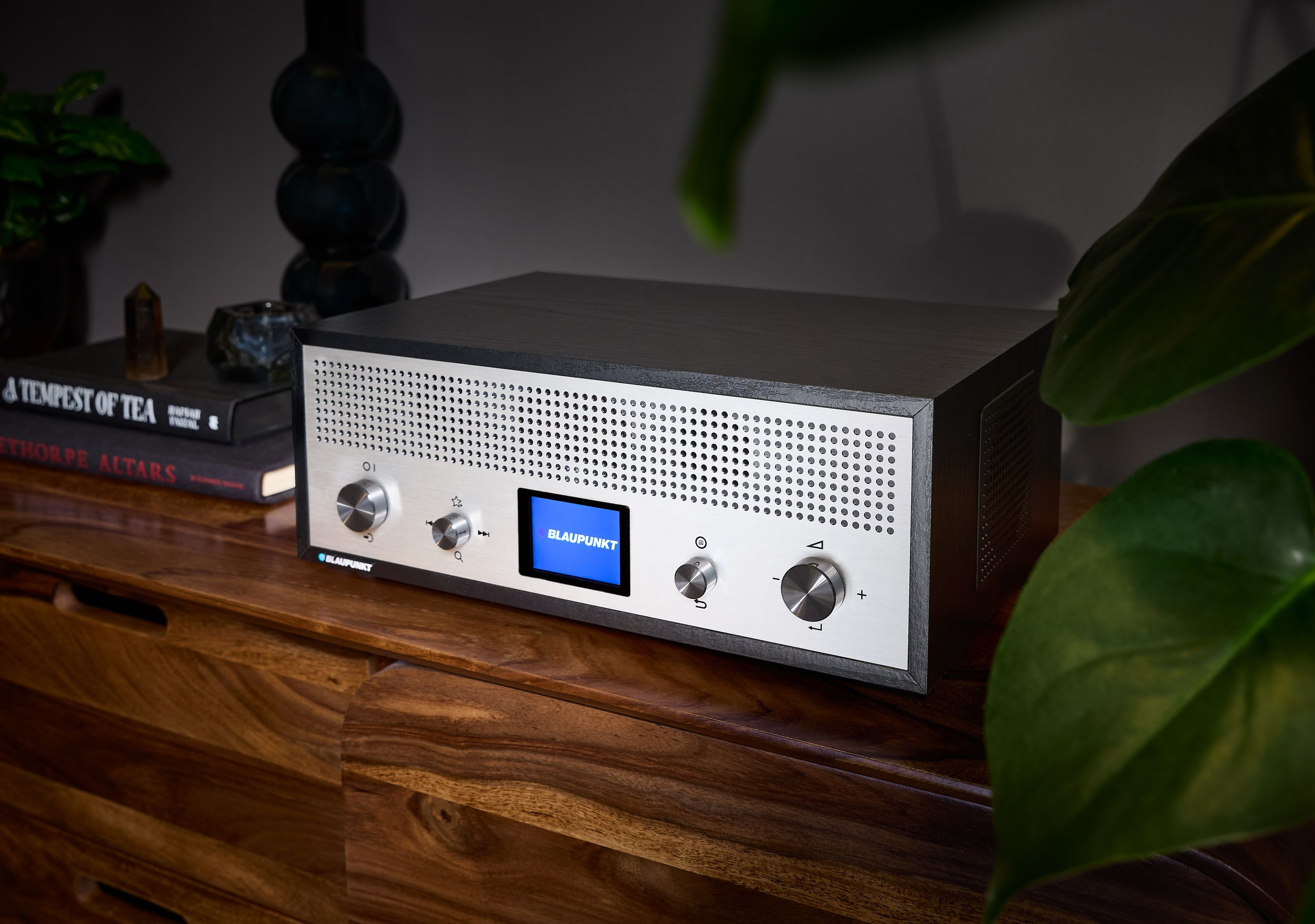 Ein Blaupunkt-Radio steht auf einem Holzschrank. Links sind Bücher und eine Pflanze. Das Radio hat einen Bildschirm und Knöpfe.