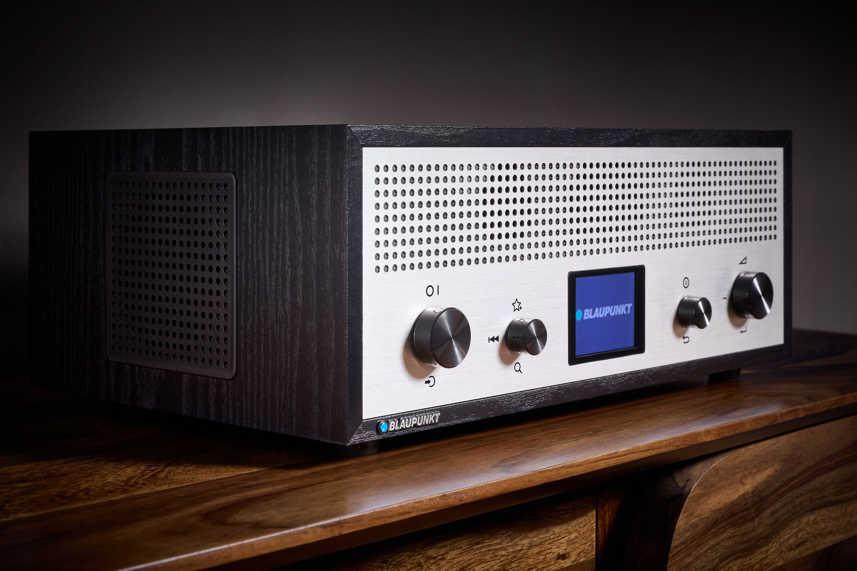 Ein Blaupunkt-Radio steht auf einem Holztisch. Es hat Knöpfe, einen Bildschirm und eine perforierte Metallfront. Dunkles Holz akzentuiert die Seiten.
