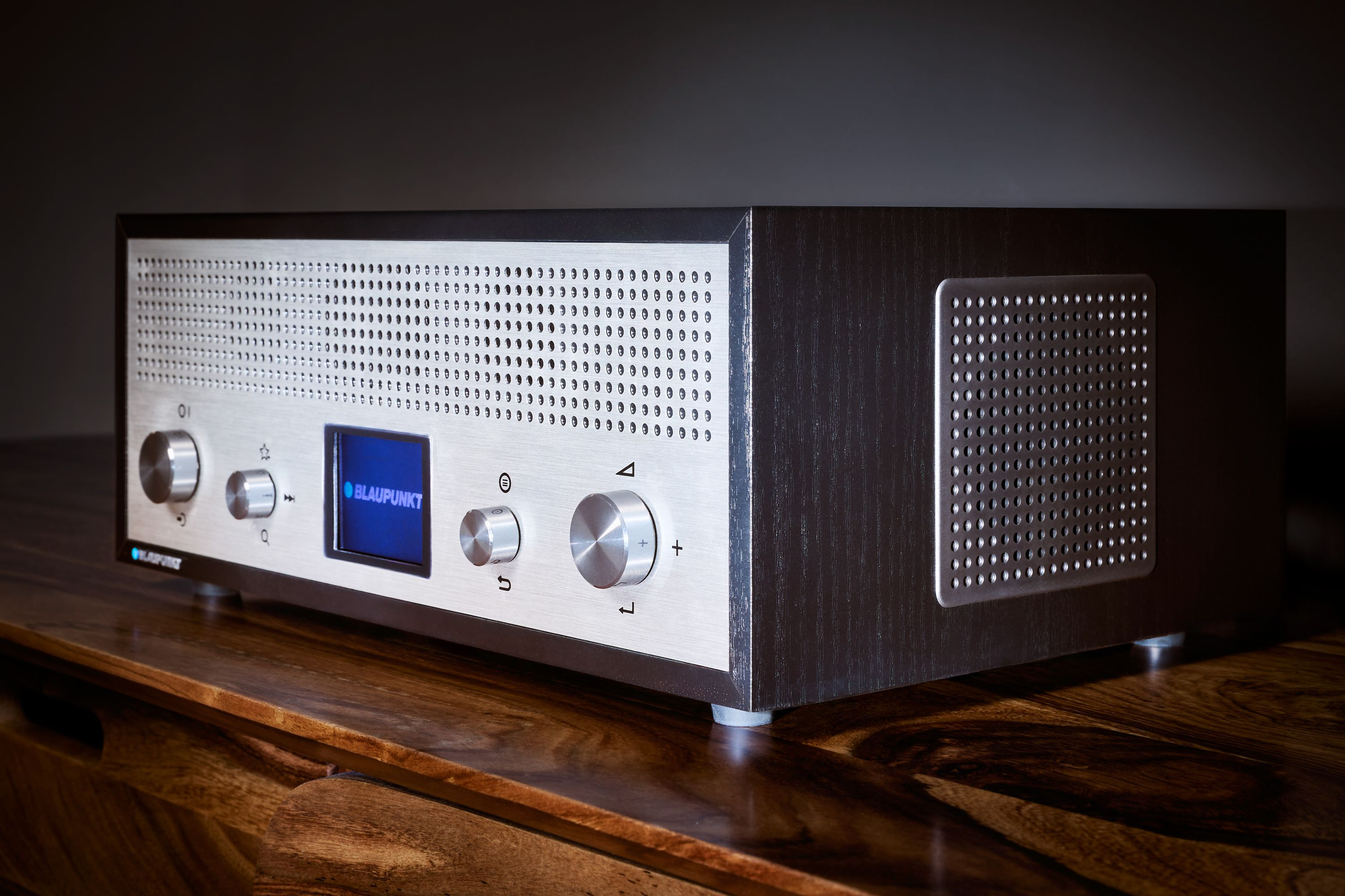 Ein Blaupunkt-Radio auf einer Holzoberfläche. Es hat eine silberne Front mit Knöpfen und einem Bildschirm. Die Seiten sind aus dunklem Holz.