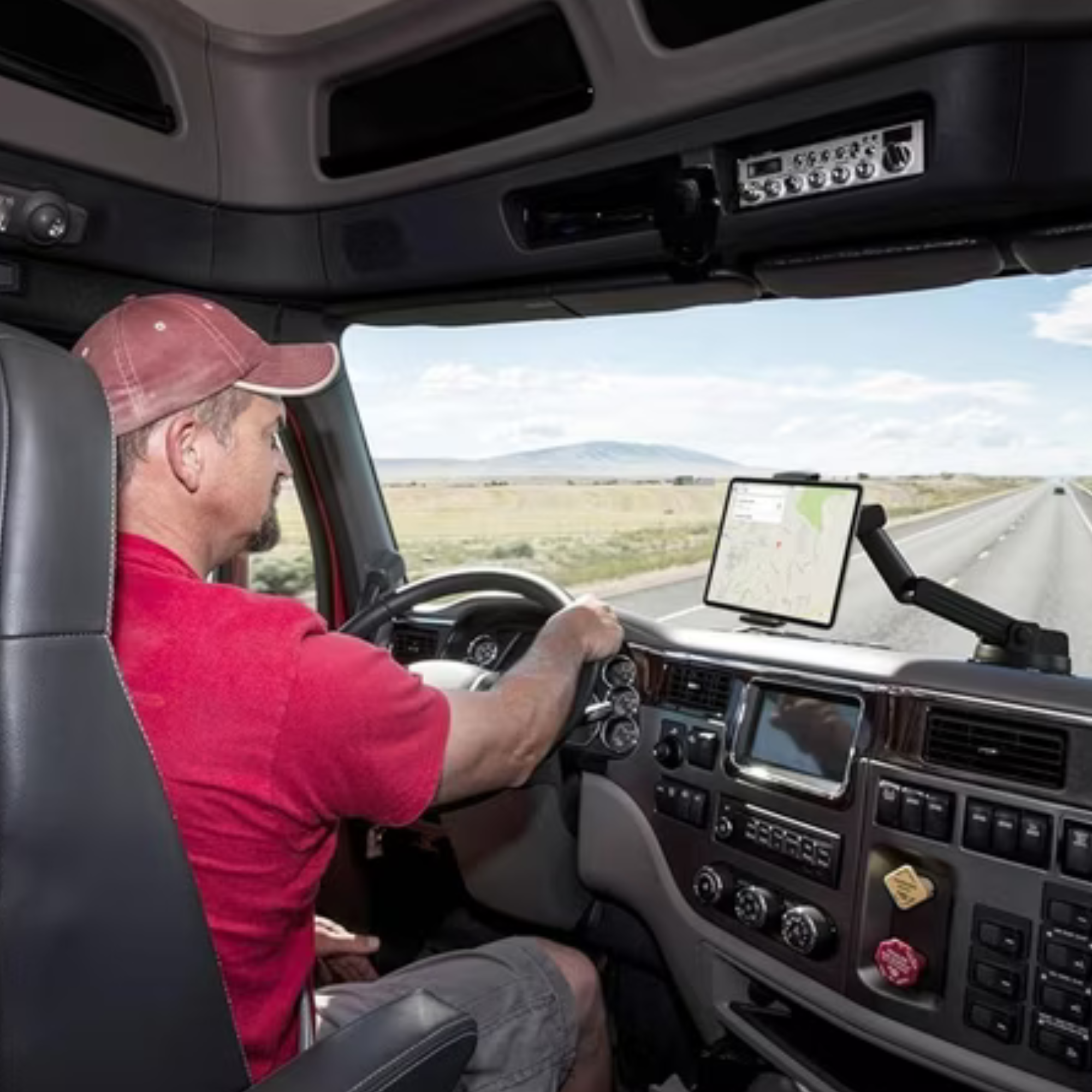In einem LKW fährt ein Mann auf einer Autobahn. Ein Tablet zeigt eine Karte an. Die Straße erstreckt sich bis zum Horizont.
