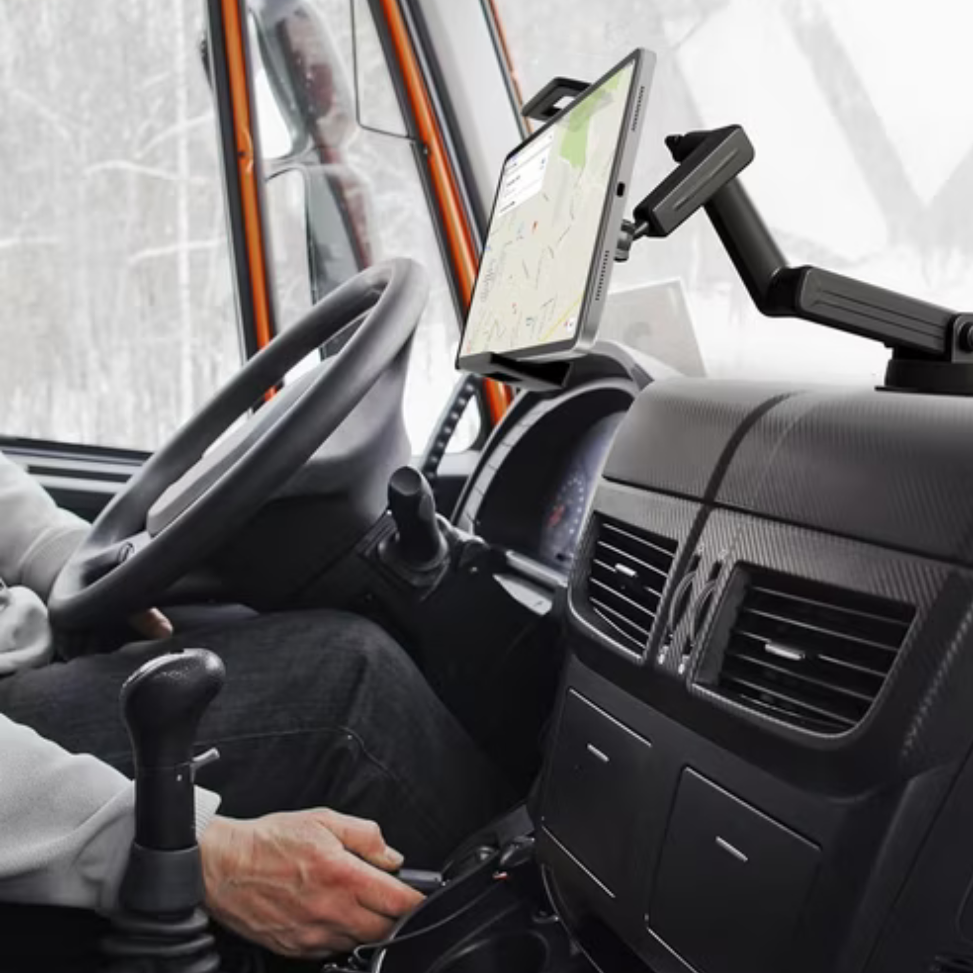 LKW-Innenansicht. Tablet mit Kartenanzeige auf dem Armaturenbrett montiert. Fahrerhände am Lenkrad und Schalthebel.