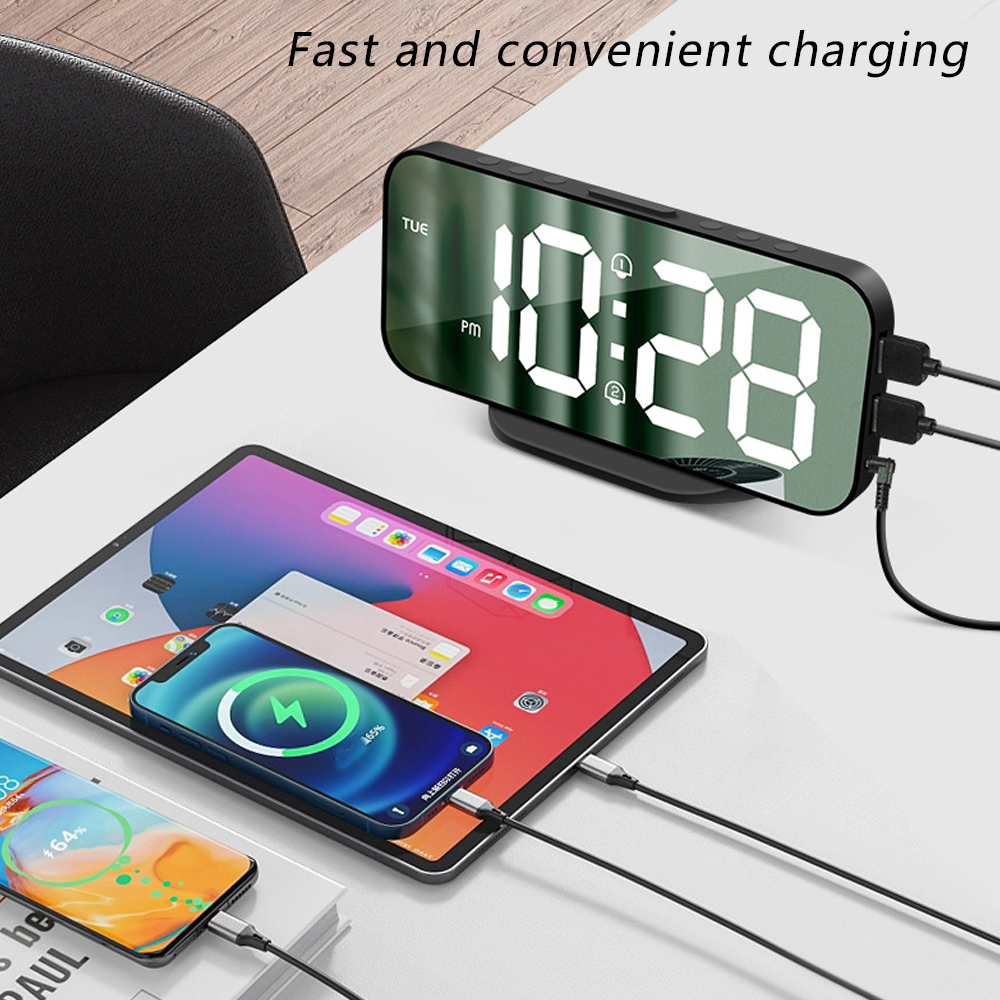 Eine Digitaluhr zeigt 10:28 an, mit ladenden Telefonen und einem Tablet. Kabel verbinden Geräte mit der Uhr und anderen Geräten.