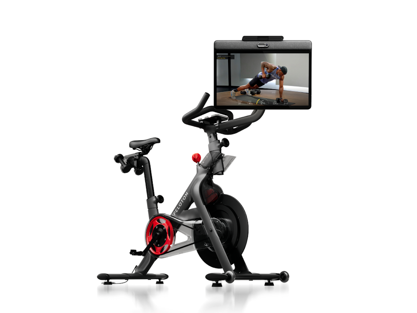 Peloton-Heimtrainer mit Bildschirm, der ein Training anzeigt. Eine Person trainiert auf dem Bildschirm. Schwarze und rote Farbakzente.
