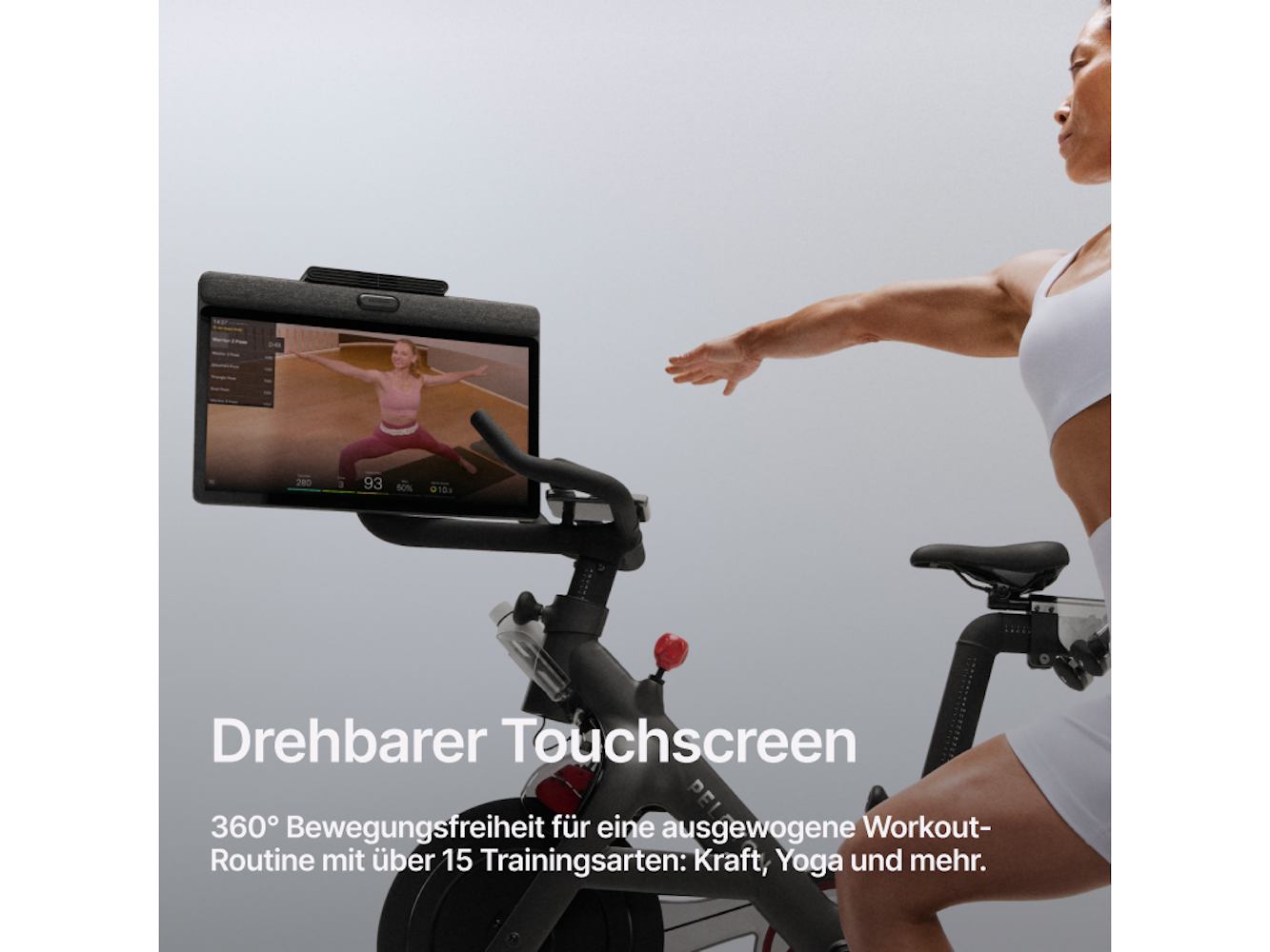 Frau auf dem Trainingsfahrrad mit Yoga-Anzeige auf dem Bildschirm. Sie greift aus. Das Fahrrad hat einen Touchscreen.