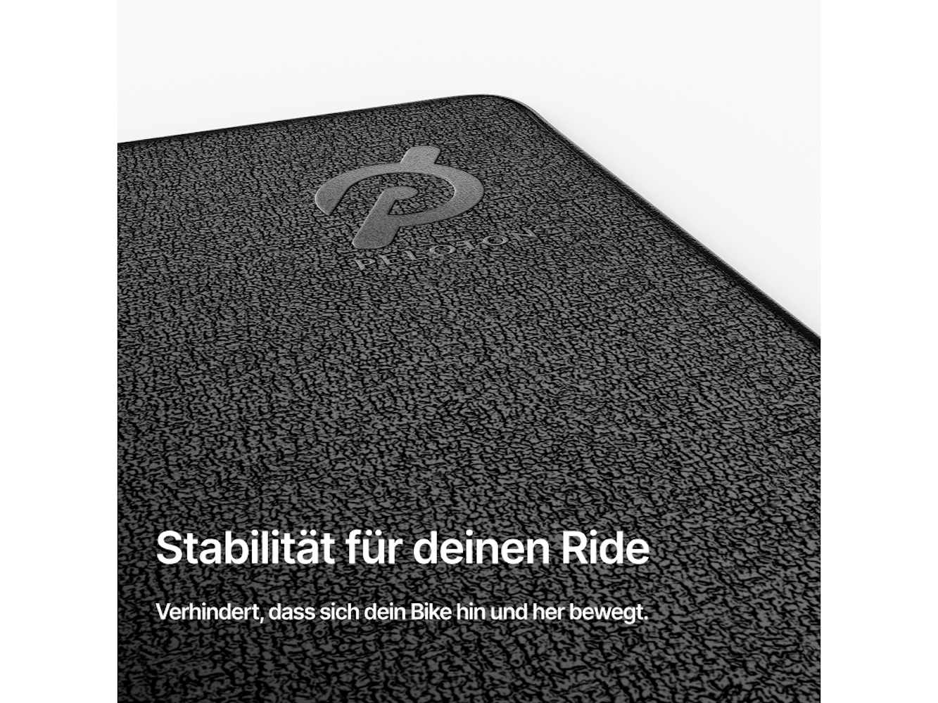 Nahaufnahme einer schwarzen strukturierten Matte mit dem Peloton-Logo. Deutscher Text: 'Stabilität für deinen Ride' und 'Verhindert Bewegungen'.