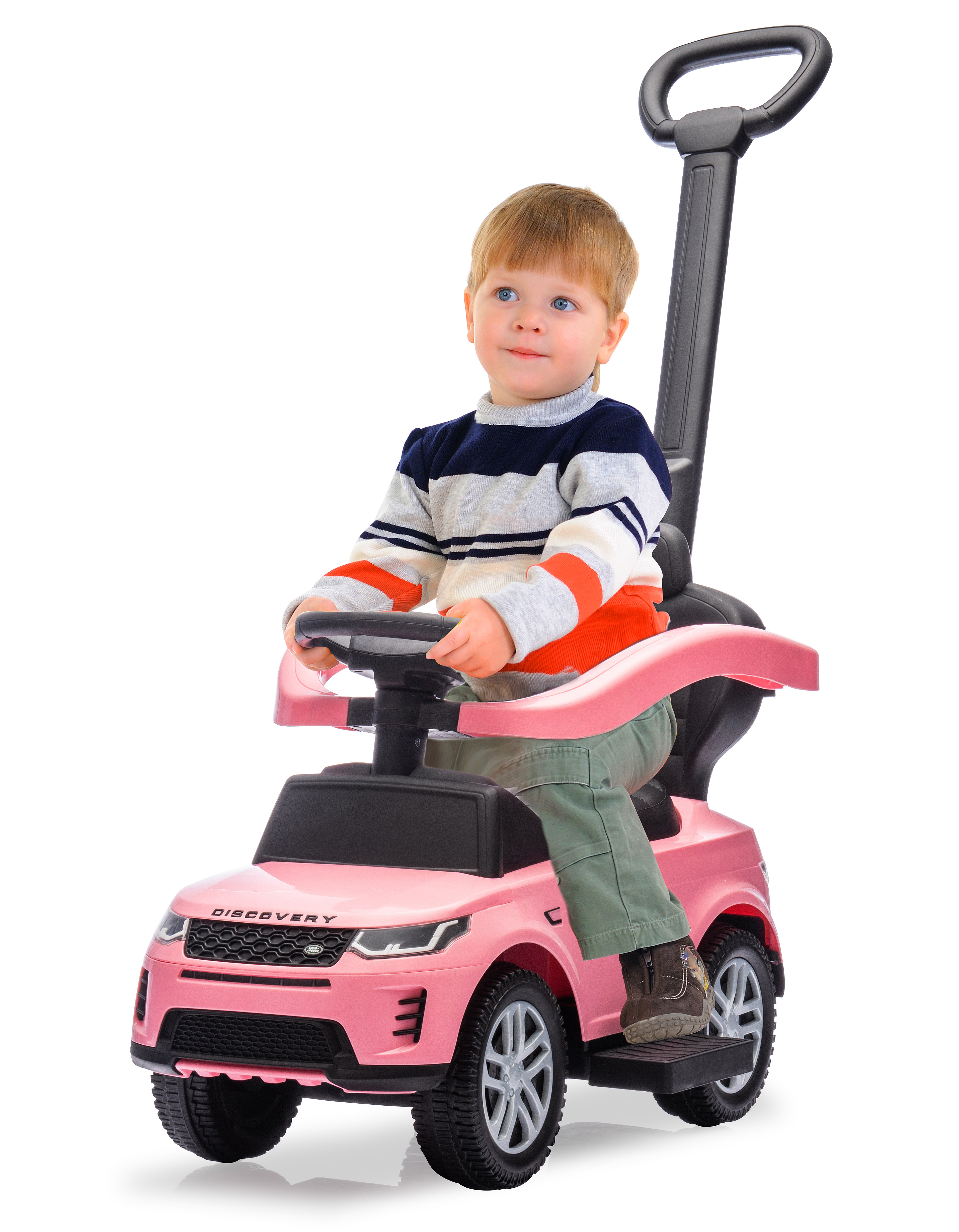 Un bambino in un'auto giocattolo rosa sorride. Indossa un maglione a righe e pantaloni verdi.