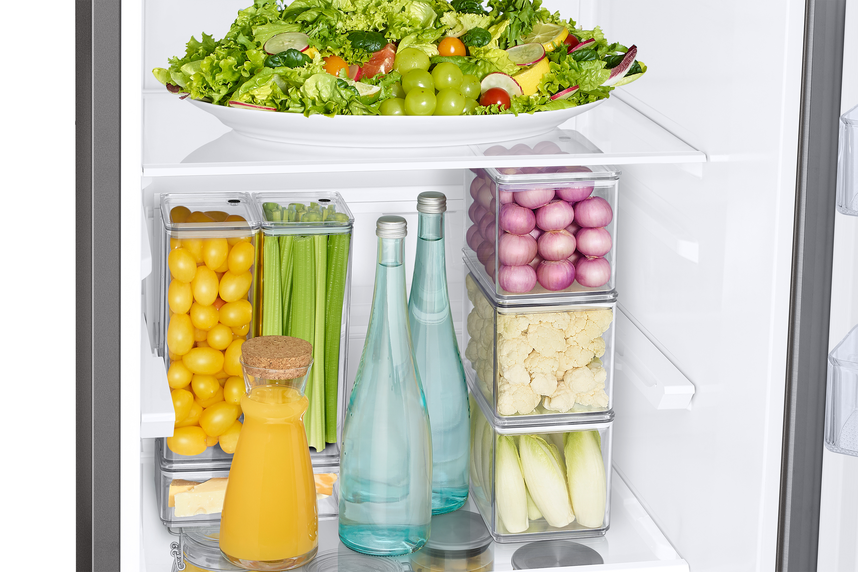 Interno del frigorifero con insalata, verdure, succo, bottiglie e contenitori di cibo. Prodotti freschi conservati ordinatamente.