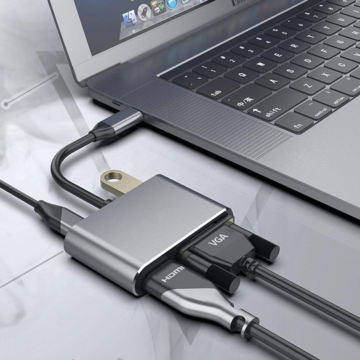 Ein Laptop, der mit einem silbernen Hub mit HDMI- und VGA-Anschlüssen verbunden ist. Kabel sind eingesteckt. Tastatur ist sichtbar. Hintergrund ist verschwommen.
