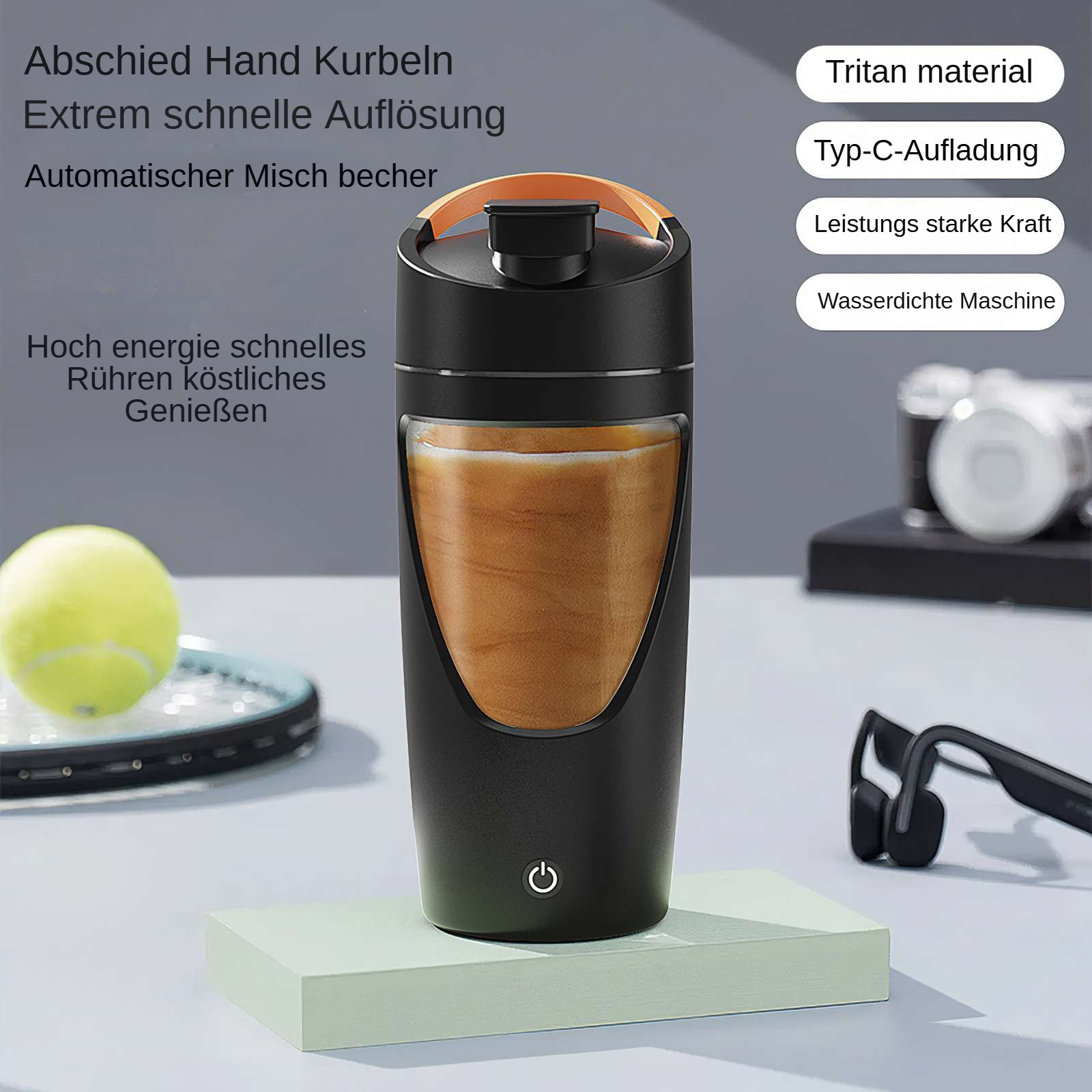 Ein schwarzer und orangefarbener Mixer mit einem Tennisball und Schläger im Hintergrund auf einem hellgrünen Block.