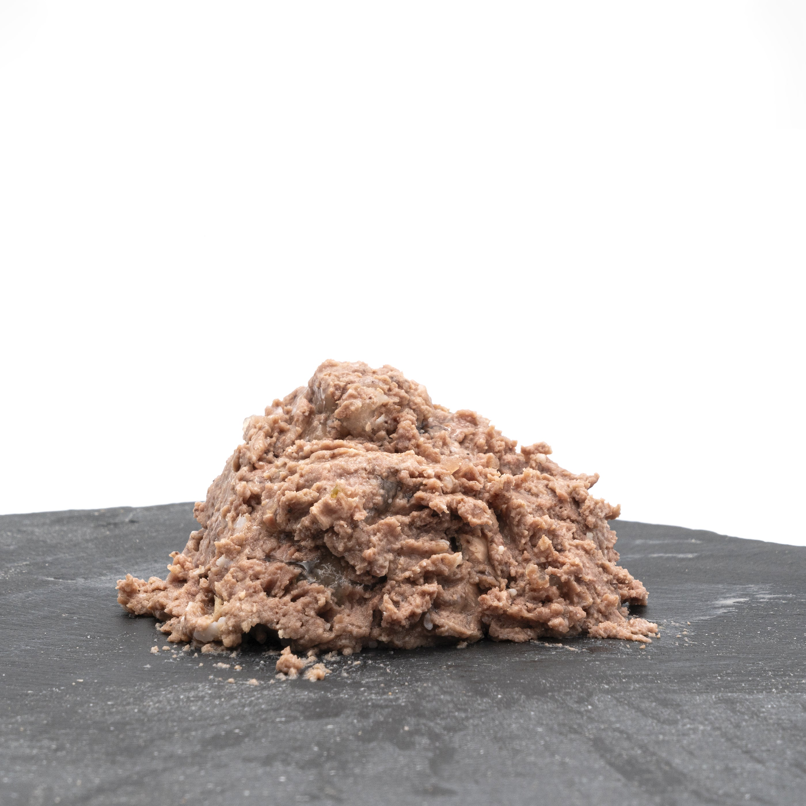 Un montón de comida húmeda para mascotas sobre una superficie gris oscuro contra un fondo blanco. La comida es marrón rosado.
