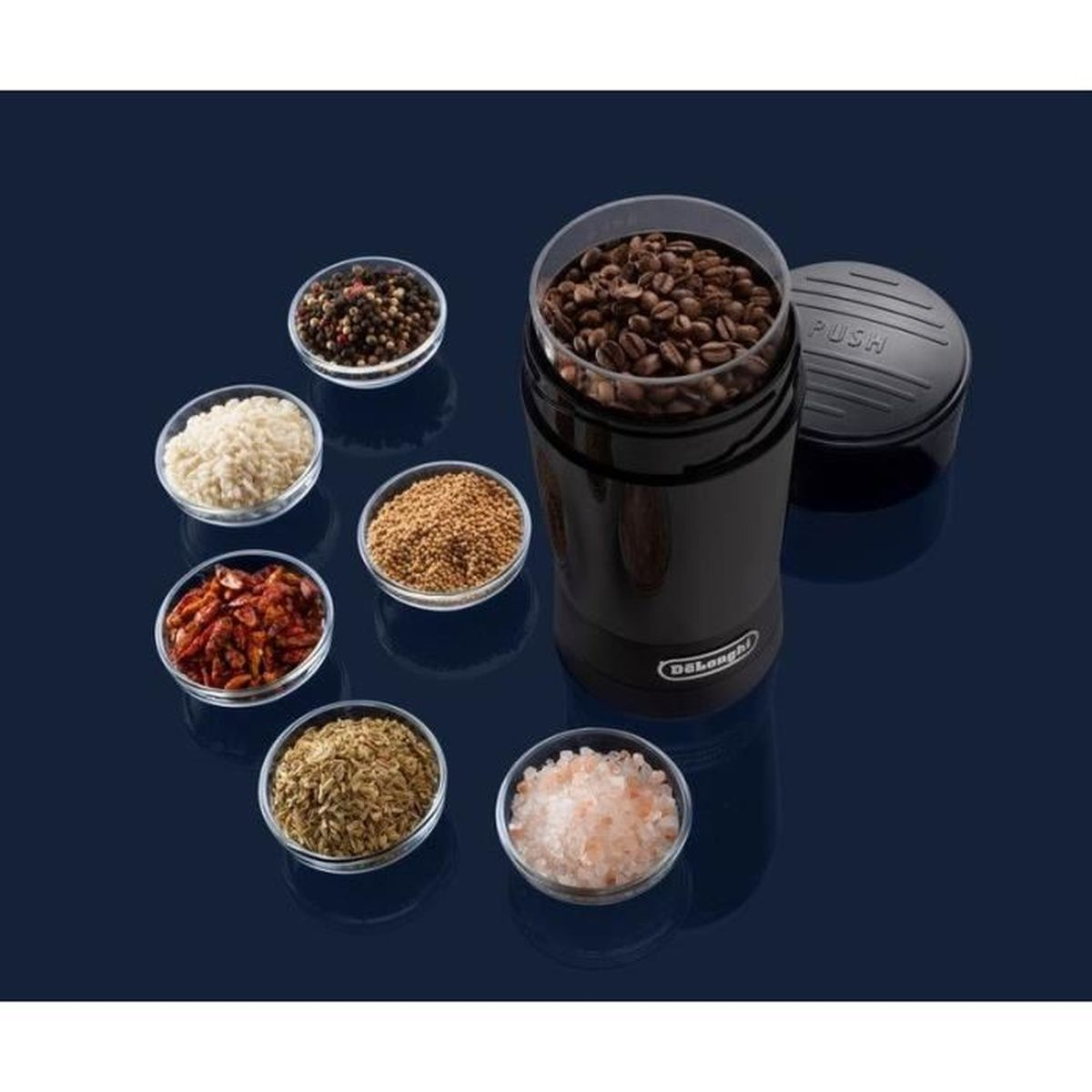 Una cafetera negra con granos de café, rodeada de pequeños cuencos con especias e ingredientes. Fondo azul oscuro.