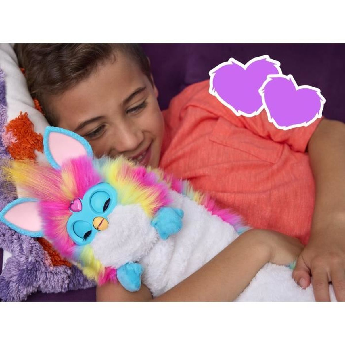 Un garçon serre dans ses bras un jouet Furby coloré. Le Furby a une fourrure arc-en-ciel, des yeux bleus et des pattes bleues. Le garçon porte une chemise orange.