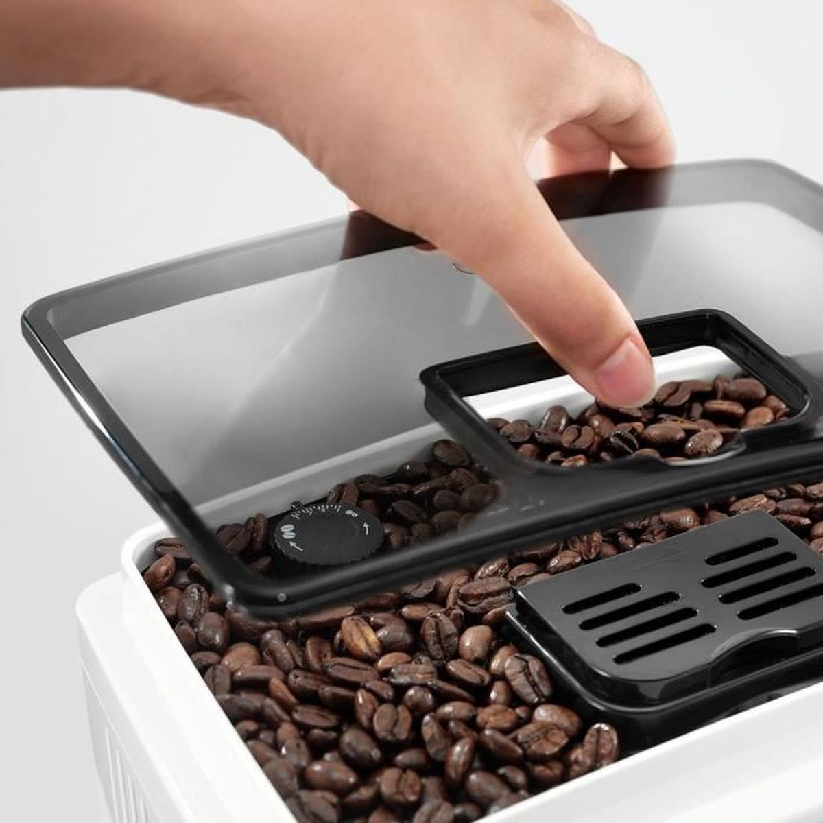 Una mano apre un contenitore di chicchi di caffè. Il contenitore è pieno di chicchi di caffè marroni. Sono visibili un quadrante nero e un piccolo vassoio nero.