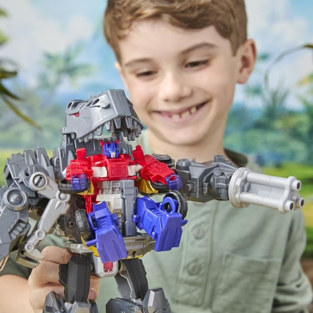 Un ragazzo sorridente tiene in mano un giocattolo Transformer. Il giocattolo è un robot dai colori rosso, blu e grigio. Lo sfondo è un'immagine verde sfocata.