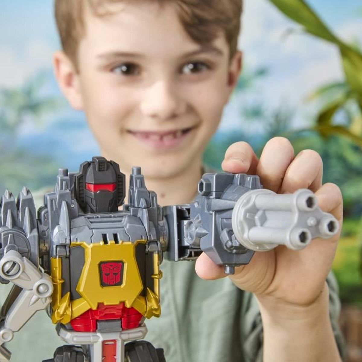 Un ragazzo tiene in mano un giocattolo Transformer grigio e oro. Il giocattolo ha un petto e una testa rossi. Il ragazzo sorride alla fotocamera.
