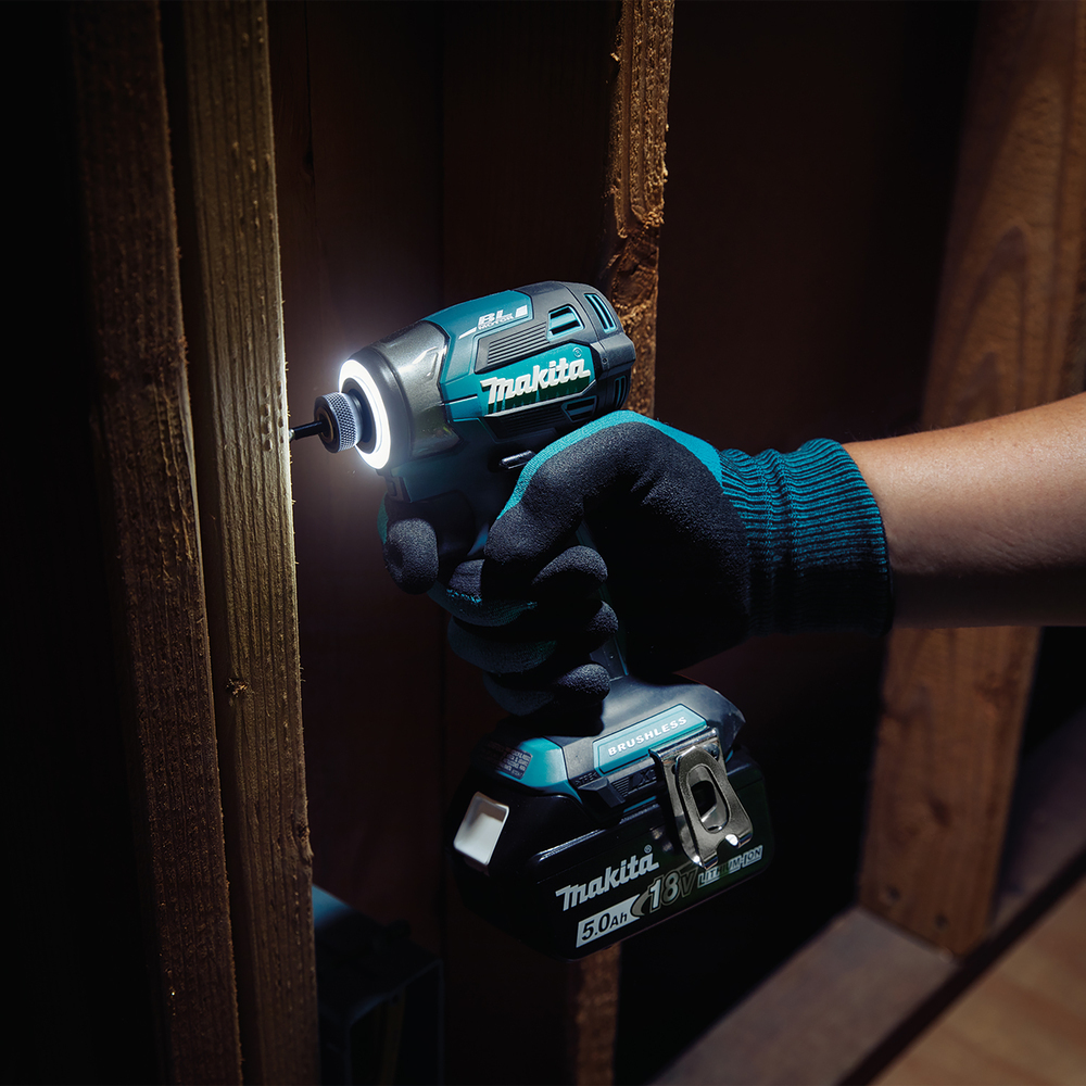 A person wearing a teal and black glove holds a Makita drill. The drill is illuminating the wooden structure it's pointed at.