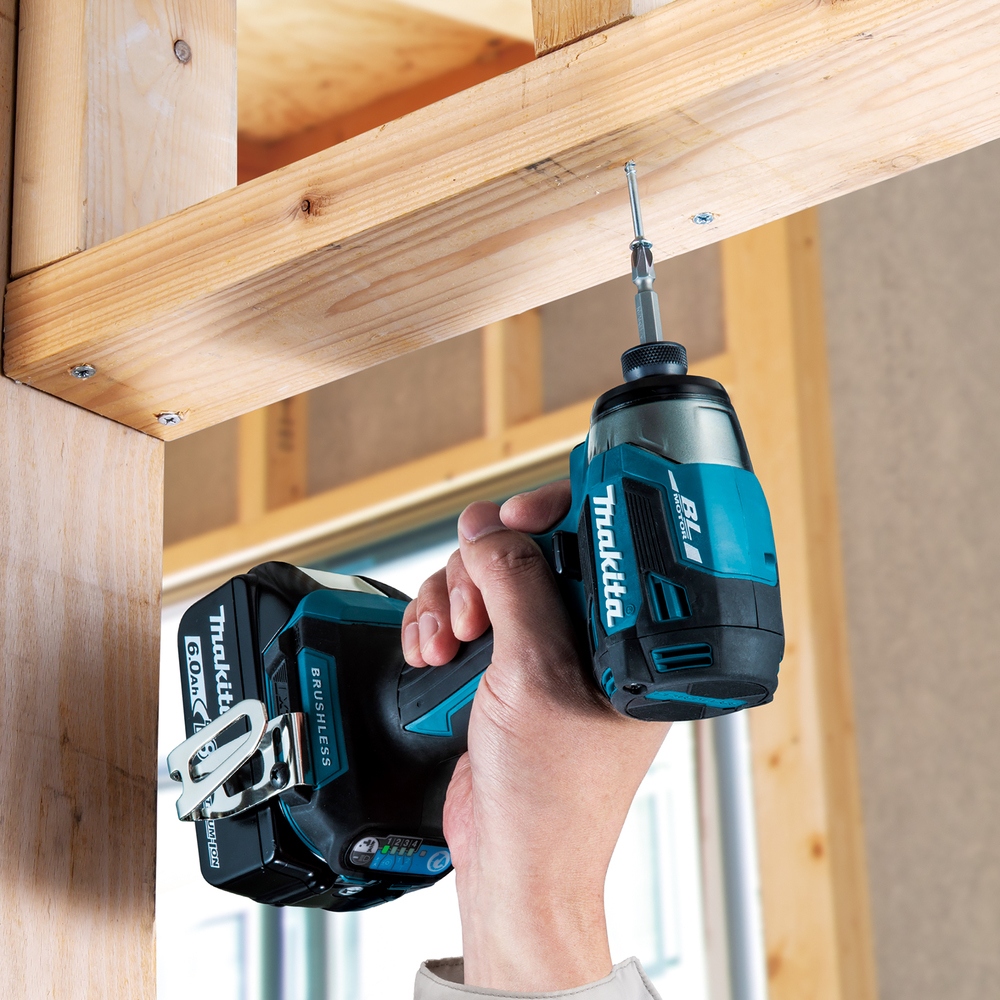A hand uses a Makita drill to screw into a wooden beam. The drill is teal and black.