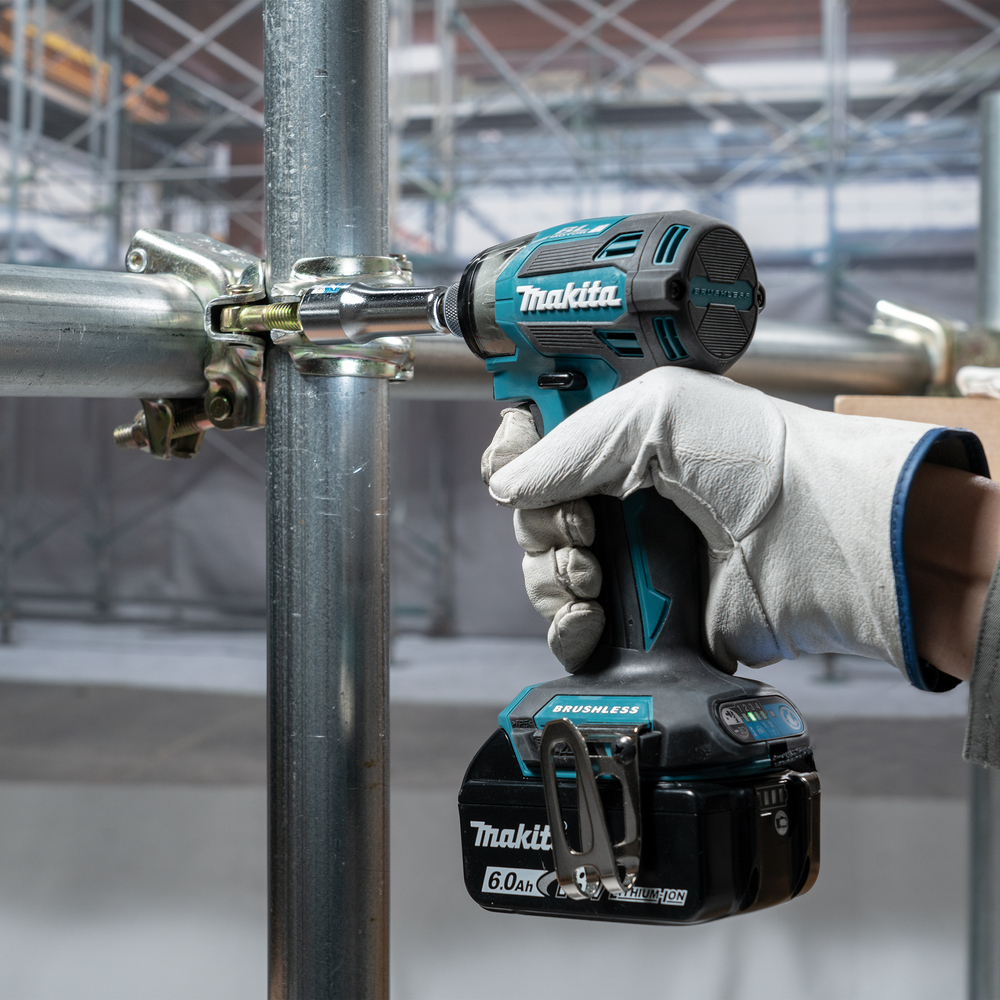 A worker wearing a glove uses a Makita impact wrench on scaffolding. The tool is teal and black. The battery is black.