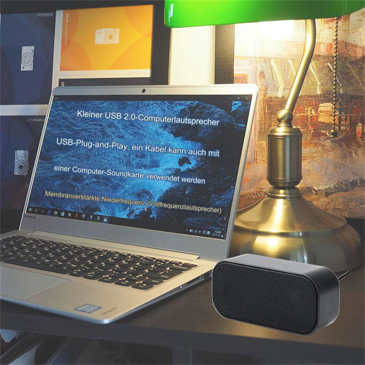 Ein Laptop zeigt deutschen Text. Daneben steht ein schwarzer Lautsprecher. Eine Lampe und dekorative Tafeln sind im Hintergrund.