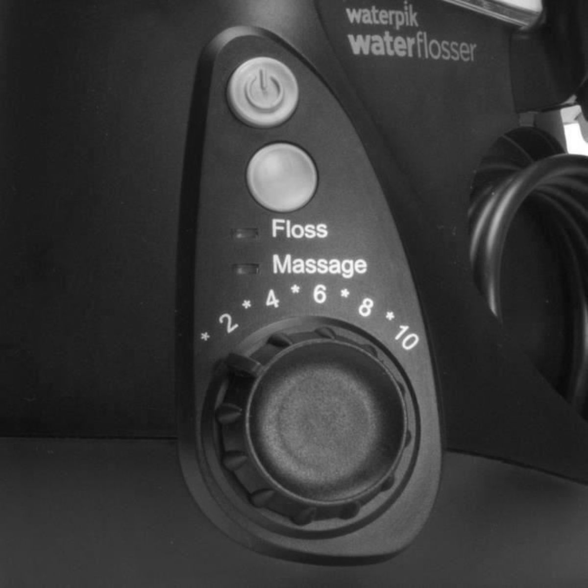 Schwarzes Waterpik-Flosser-Bedienfeld. Enthält Ein-/Ausschalter, Modustasten, Intensitätsregler mit Zahlen 2-10 und Text 'Floss' und 'Massage'.