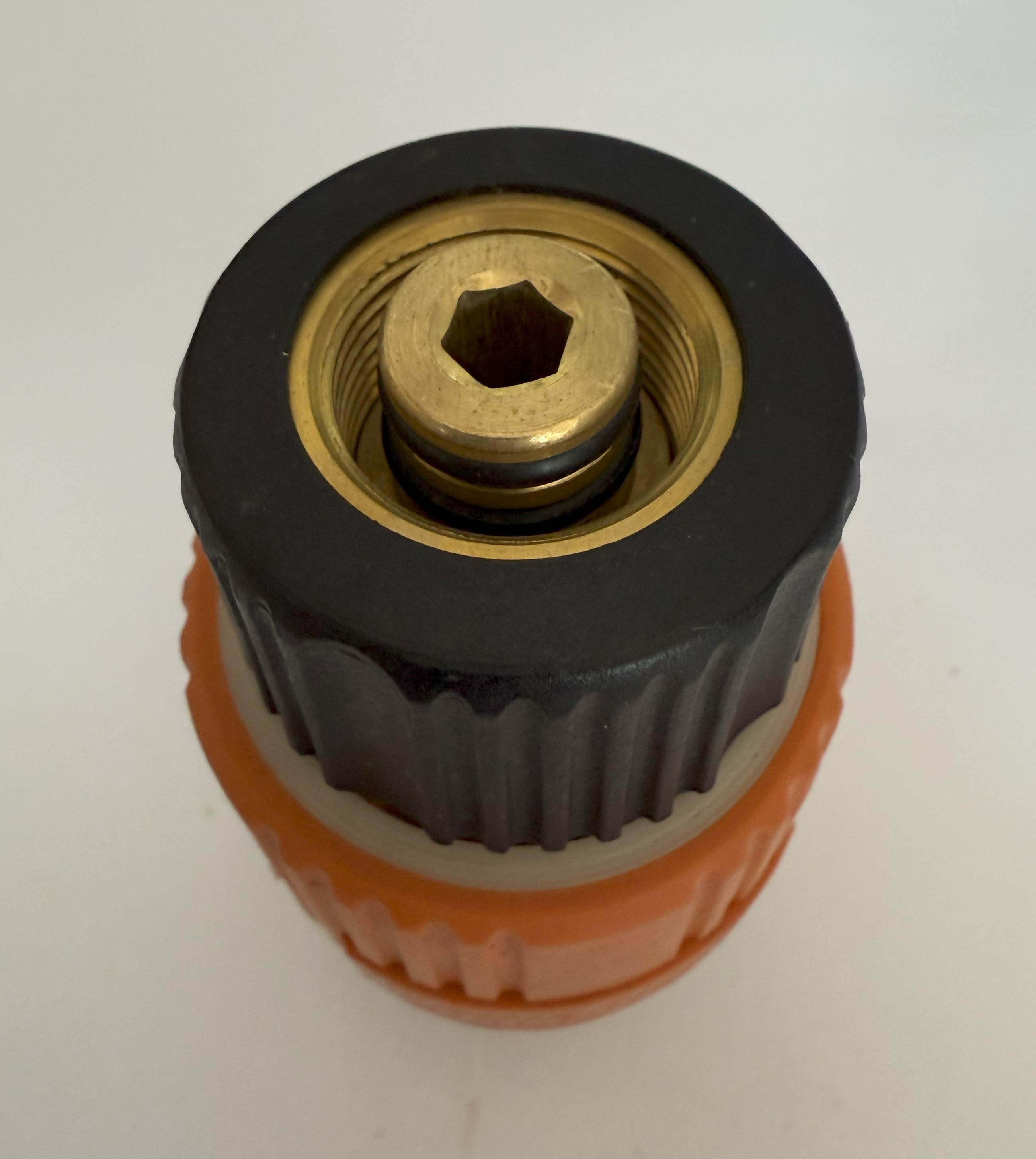 Nahaufnahme eines Schlauchanschlusses. Er hat einen schwarzen Deckel, einen orangefarbenen Sockel und eine Messingmitte mit sechseckiger Öffnung. Weißer Hintergrund.