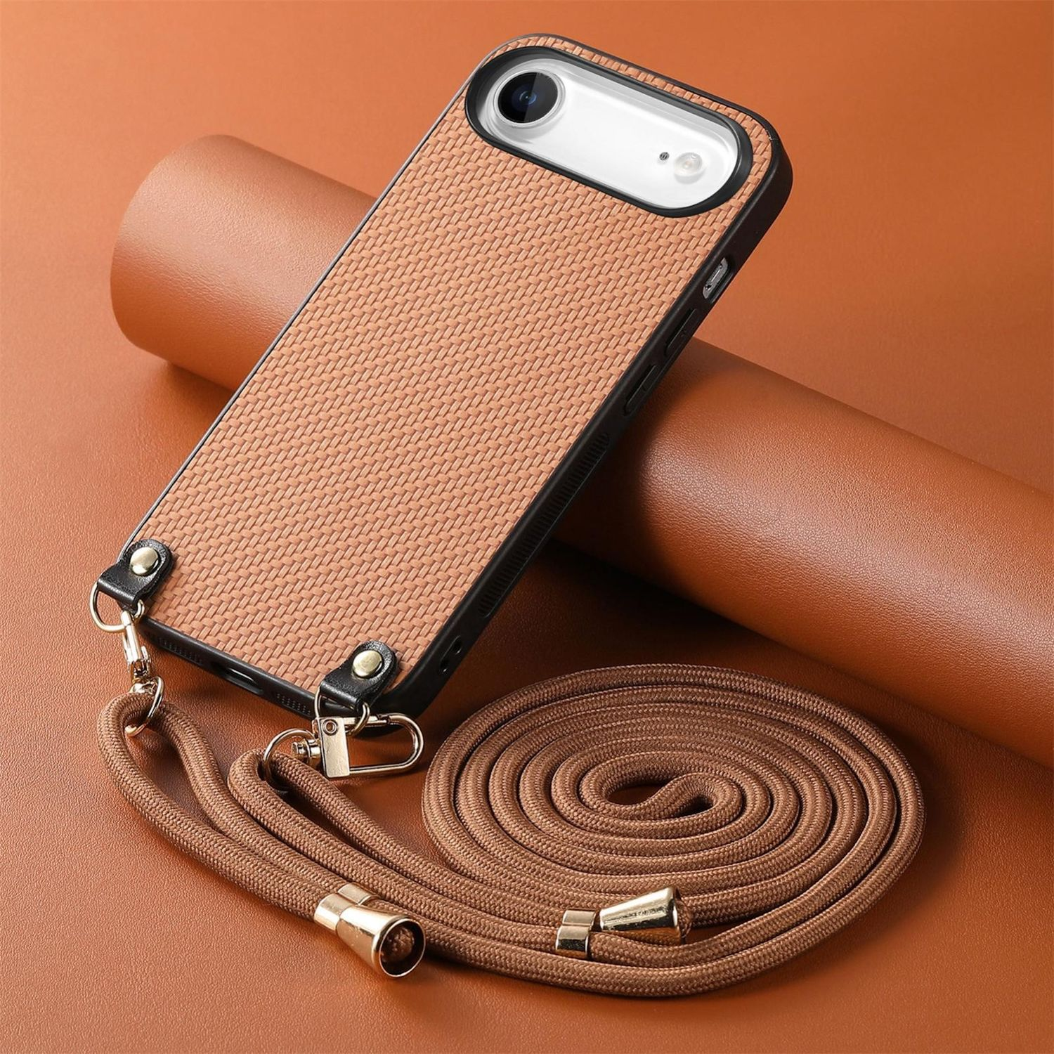 Una funda de teléfono marrón claro con correa, sobre una superficie marrón. La funda tiene una textura tejida. La correa está enrollada junto a la funda.