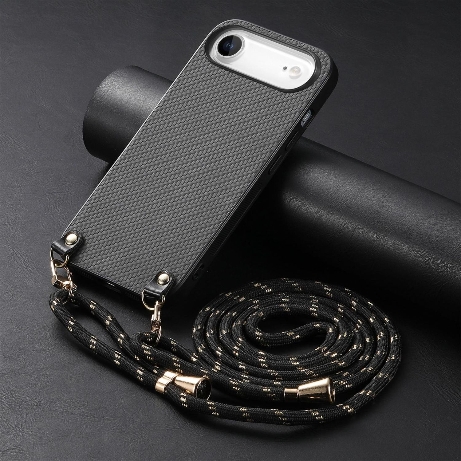 Funda de teléfono negra con cordón, sobre una superficie negra. El cordón es negro con detalles dorados. Un cilindro negro detrás del teléfono.