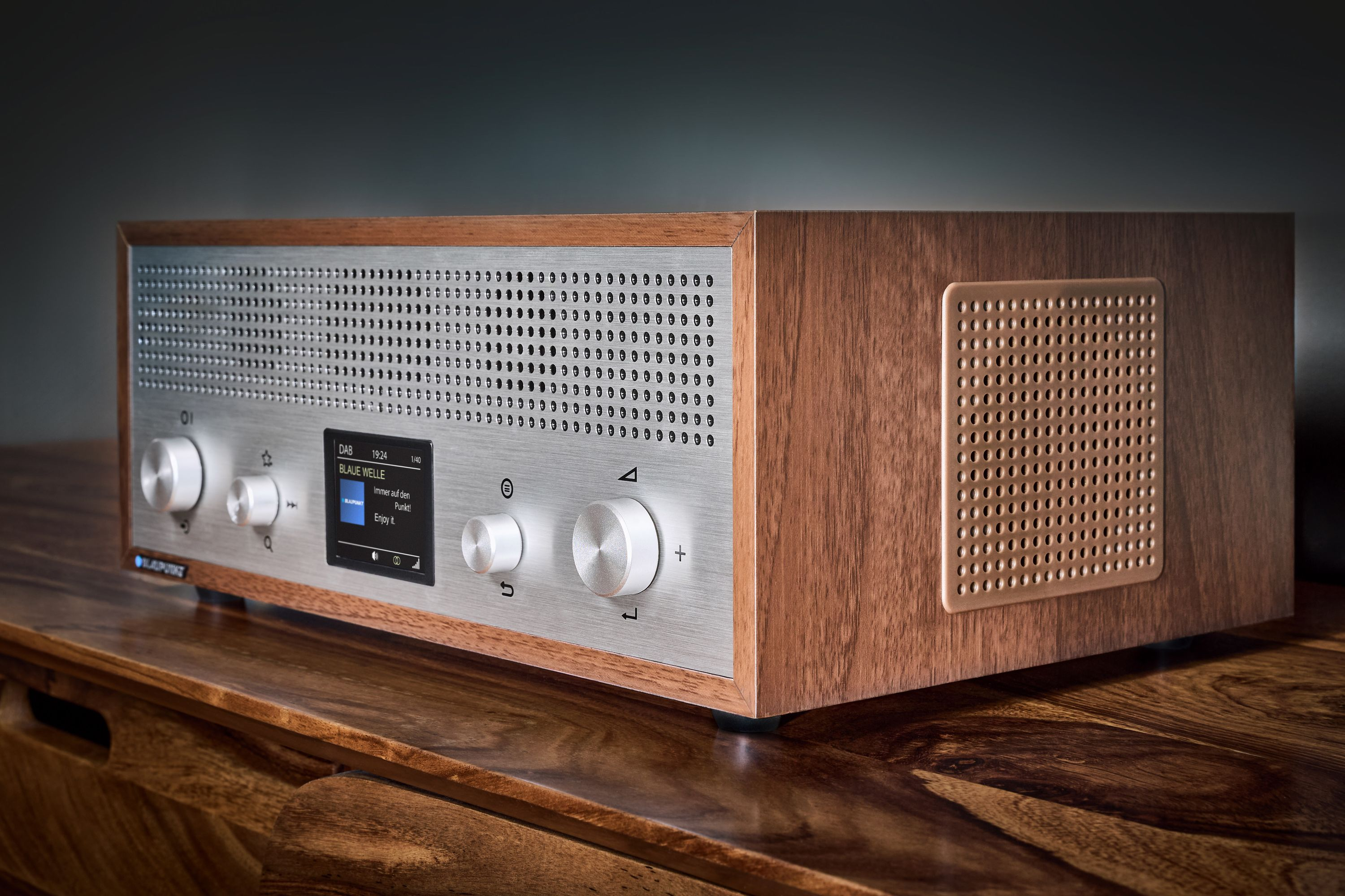 Ein Holzradio mit Metallfront. Es zeigt Informationen auf einem Bildschirm an. Knöpfe und Tasten sind sichtbar.