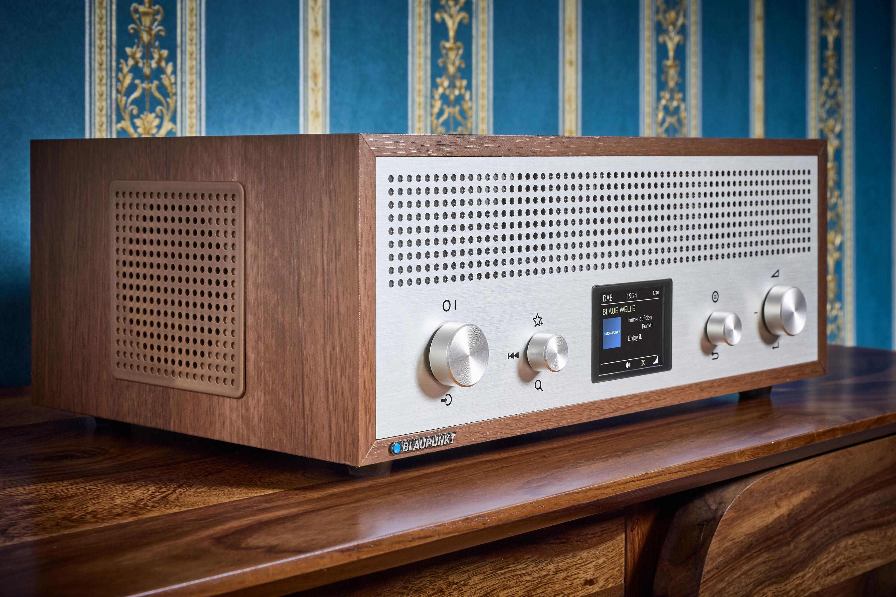 Ein braunes und silbernes Blaupunkt-Radio auf einer Holzoberfläche. Der Hintergrund hat eine blau-goldene Tapete.