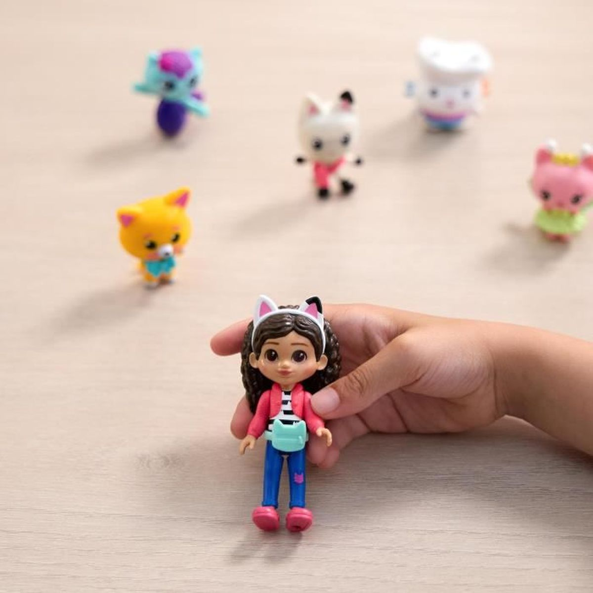 Ein Kinderhand hält eine Puppe mit Katzenohren. Andere Figuren mit Katzenmotiven sind im Hintergrund.