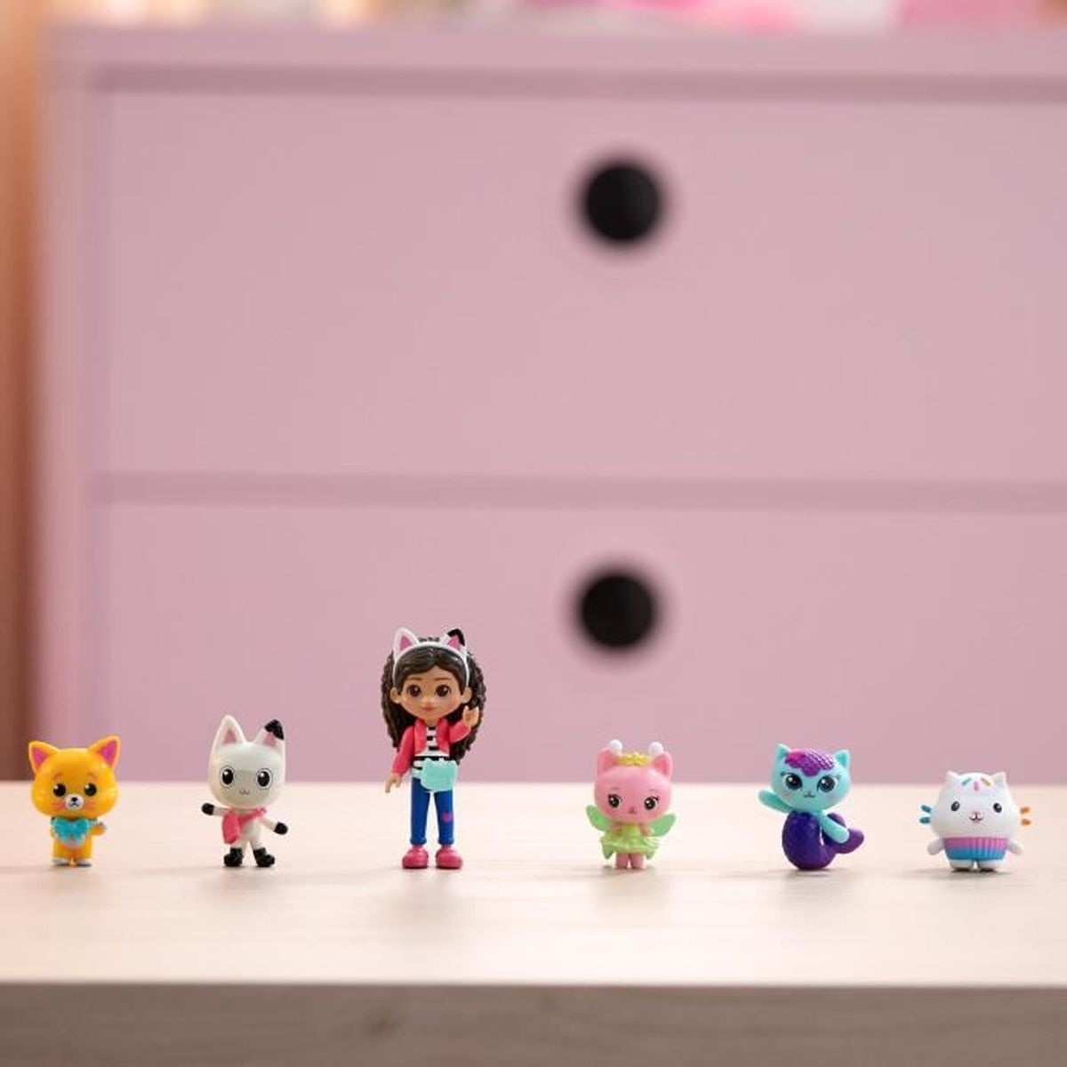 Reihe von Gabby's Puppenhaus-Figuren auf einem Tisch. Im Hintergrund befindet sich eine rosa Kommode.